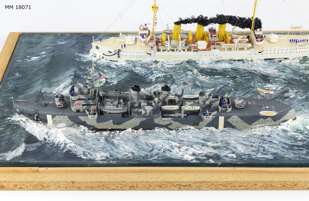 Fartygsdiorama visande två fartyg under gång till sjöss. Modellen är tillverkad av trä med detaljer av plast, papper och metall. Modellerna är placerade i ett hav av någon form av plastelina, målat i gröna och blå toner. Havet är uppbyggt på en rektangulär platta. Modellerna är detaljerat återgivna och visar pansarkryssaren "Fylgia", den ena modellen visar fartyget i sitt ursprungliga skick, den andra modellen visar fartyget efter moderniseringen 1939-40. Den "äldre" modellen visar ett vitt fartyg med rök bestående av grå ull från de tre skorstenarna, den "yngre" modellen visar ett kamouflagemålat fartyg försett med vitt neutralitetsband. Dioramat är signerat på havet med rött: "H Biärsjö".
