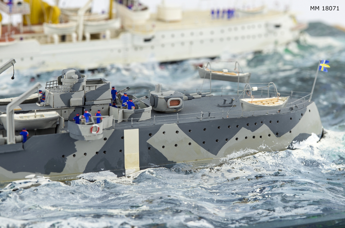 Fartygsdiorama visande två fartyg under gång till sjöss. Modellen är tillverkad av trä med detaljer av plast, papper och metall. Modellerna är placerade i ett hav av någon form av plastelina, målat i gröna och blå toner. Havet är uppbyggt på en rektangulär platta. Modellerna är detaljerat återgivna och visar pansarkryssaren "Fylgia", den ena modellen visar fartyget i sitt ursprungliga skick, den andra modellen visar fartyget efter moderniseringen 1939-40. Den "äldre" modellen visar ett vitt fartyg med rök bestående av grå ull från de tre skorstenarna, den "yngre" modellen visar ett kamouflagemålat fartyg försett med vitt neutralitetsband. Dioramat är signerat på havet med rött: "H Biärsjö".