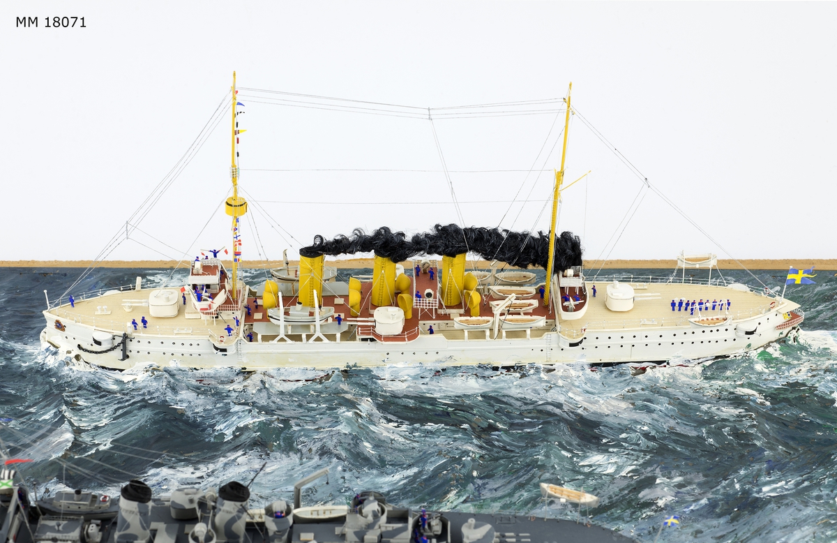 Fartygsdiorama visande två fartyg under gång till sjöss. Modellen är tillverkad av trä med detaljer av plast, papper och metall. Modellerna är placerade i ett hav av någon form av plastelina, målat i gröna och blå toner. Havet är uppbyggt på en rektangulär platta. Modellerna är detaljerat återgivna och visar pansarkryssaren "Fylgia", den ena modellen visar fartyget i sitt ursprungliga skick, den andra modellen visar fartyget efter moderniseringen 1939-40. Den "äldre" modellen visar ett vitt fartyg med rök bestående av grå ull från de tre skorstenarna, den "yngre" modellen visar ett kamouflagemålat fartyg försett med vitt neutralitetsband. Dioramat är signerat på havet med rött: "H Biärsjö".