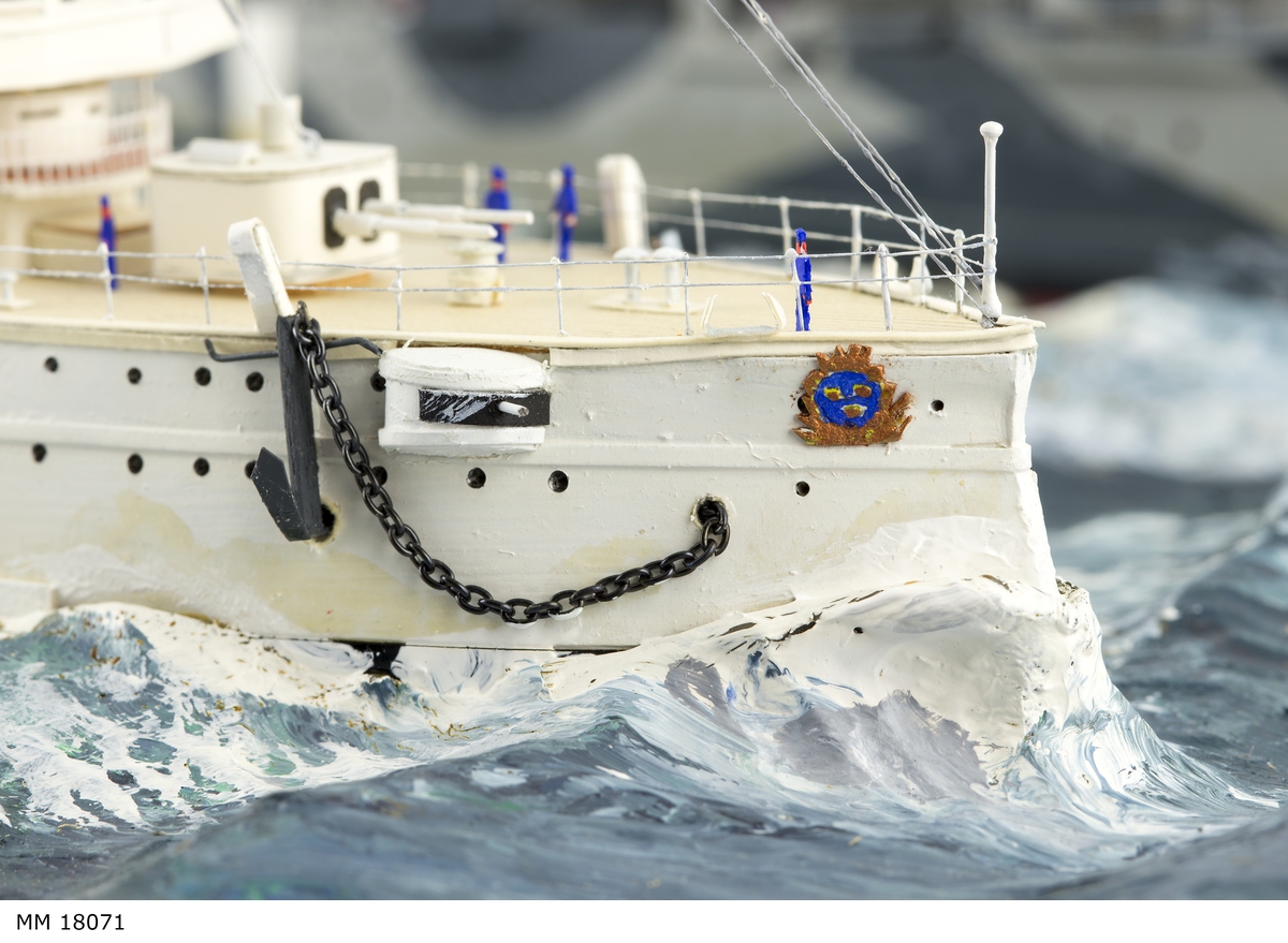 Fartygsdiorama visande två fartyg under gång till sjöss. Modellen är tillverkad av trä med detaljer av plast, papper och metall. Modellerna är placerade i ett hav av någon form av plastelina, målat i gröna och blå toner. Havet är uppbyggt på en rektangulär platta. Modellerna är detaljerat återgivna och visar pansarkryssaren "Fylgia", den ena modellen visar fartyget i sitt ursprungliga skick, den andra modellen visar fartyget efter moderniseringen 1939-40. Den "äldre" modellen visar ett vitt fartyg med rök bestående av grå ull från de tre skorstenarna, den "yngre" modellen visar ett kamouflagemålat fartyg försett med vitt neutralitetsband. Dioramat är signerat på havet med rött: "H Biärsjö".