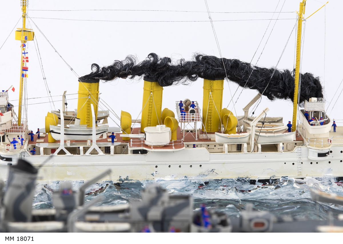 Fartygsdiorama visande två fartyg under gång till sjöss. Modellen är tillverkad av trä med detaljer av plast, papper och metall. Modellerna är placerade i ett hav av någon form av plastelina, målat i gröna och blå toner. Havet är uppbyggt på en rektangulär platta. Modellerna är detaljerat återgivna och visar pansarkryssaren "Fylgia", den ena modellen visar fartyget i sitt ursprungliga skick, den andra modellen visar fartyget efter moderniseringen 1939-40. Den "äldre" modellen visar ett vitt fartyg med rök bestående av grå ull från de tre skorstenarna, den "yngre" modellen visar ett kamouflagemålat fartyg försett med vitt neutralitetsband. Dioramat är signerat på havet med rött: "H Biärsjö".