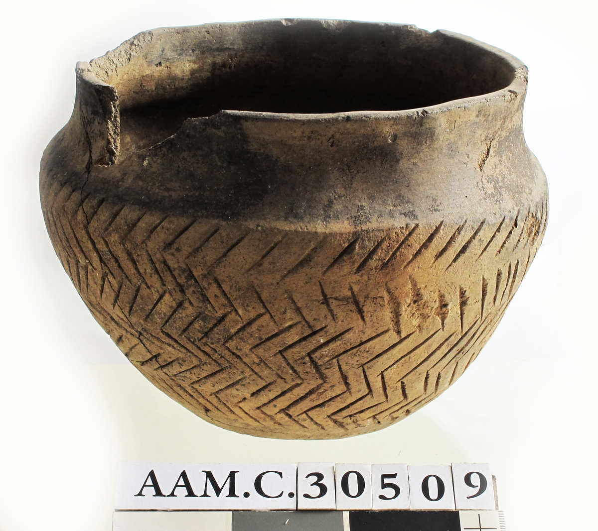 Leirkar av lyst brunlig, temmelig tykt, godt brent gods av form nærmest som Bøe: Keramikk, fig. 11, men med skarpere markert skulder og sterkere skrådd mot bunnen, sml. fig. 10. Randen er rett avskåret, ikke fortykket. Halsen er glatt, sidene er ornert med dypt innrissete streker i fiskebeinsmønster. Orneringen er noe skjødesløst utført, men meget virkningsfull. Noen skår i randen mangler, ellers utmerket bevart.