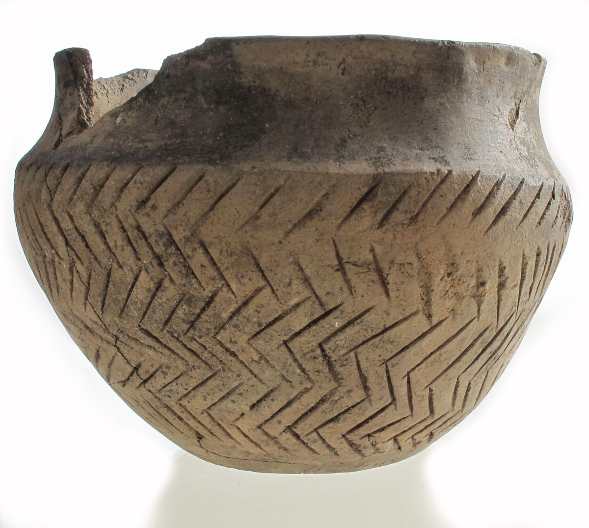 Leirkar av lyst brunlig, temmelig tykt, godt brent gods av form nærmest som Bøe: Keramikk, fig. 11, men med skarpere markert skulder og sterkere skrådd mot bunnen, sml. fig. 10. Randen er rett avskåret, ikke fortykket. Halsen er glatt, sidene er ornert med dypt innrissete streker i fiskebeinsmønster. Orneringen er noe skjødesløst utført, men meget virkningsfull. Noen skår i randen mangler, ellers utmerket bevart.