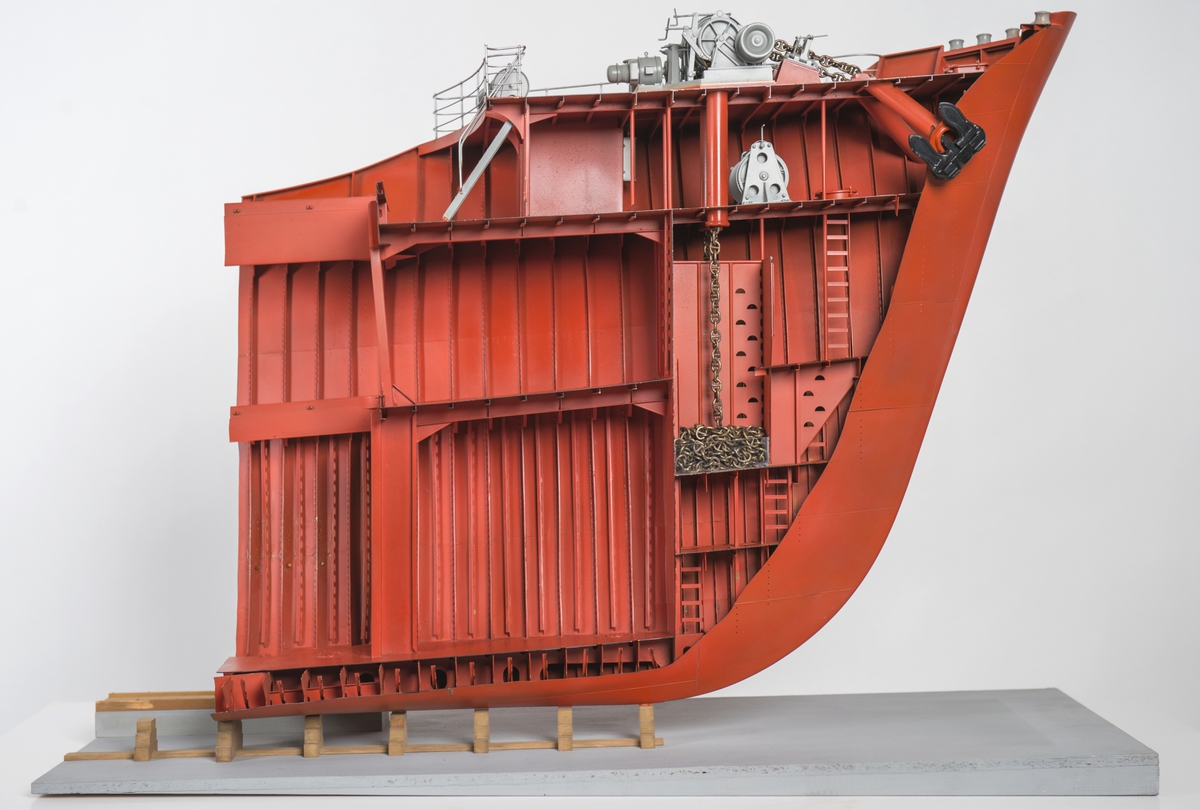 Modell av förskepp, från förstäv till mitten av l:ans lucka, byggd av metall, styrbords sida borttagen, visande konstruktionen med bottenstockar, spant, tanktak, skott och däck. Helt rödmålad. På backen gråmålat ankarspel och wirerullar. Under backen stor wirerulle. Två svarta ankare, stuvade i kättingbox.