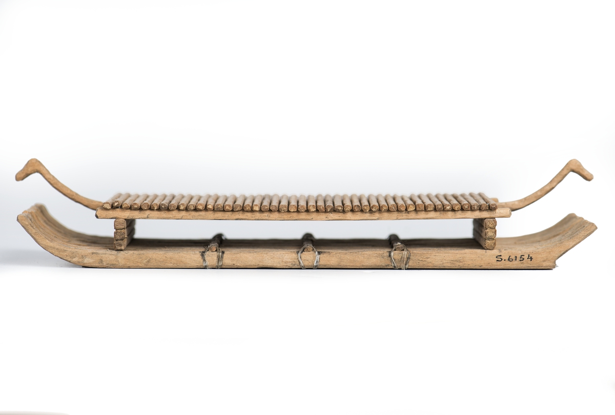 Modell av flotte, rekonstruktion av "Bredarörtypen", skeppsbild från Bredarör invid Kivik, Skåne. Flytkropp av 9 raka, i ändarna svagt uppböjda stockar, sammanhållna av 3 tvärbalkar och två plattformsstöttor. Plattformen består av tvärgående ribbor uppburna av tre längsgående spärrar varav den mittersta, utskjutande, avslutas med djurhuvud. Skala: 1/60 (Jfr. S.5892 = skala 1/50).