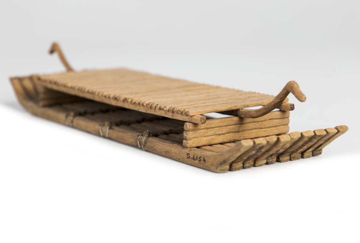 Modell av flotte, rekonstruktion av "Bredarörtypen", skeppsbild från Bredarör invid Kivik, Skåne. Flytkropp av 9 raka, i ändarna svagt uppböjda stockar, sammanhållna av 3 tvärbalkar och två plattformsstöttor. Plattformen består av tvärgående ribbor uppburna av tre längsgående spärrar varav den mittersta, utskjutande, avslutas med djurhuvud. Skala: 1/60 (Jfr. S.5892 = skala 1/50).