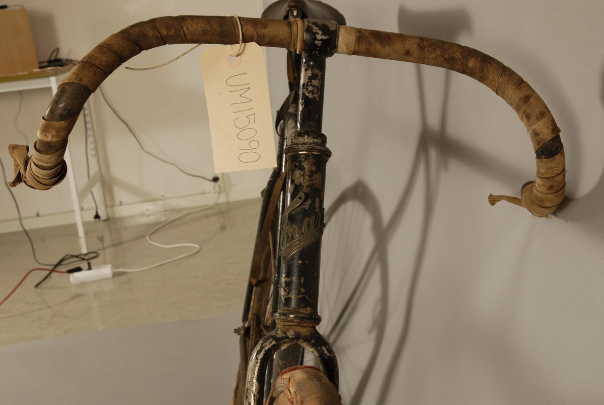Racer. Svart. Fälgarna av trä. Den främre gulmålad. Sadeln av svart läder. Läderrem fastbunden mellan ram och sadel. Styret delvis inlindat med ljust bomullsband. Märkt: Fram. Akt. Bol. Josef Eriksson, Velocipedfabrik, Uppsala. Sadeln märkt Brooks. På ramen handskriven text: Cyklist Ragge Malm.
