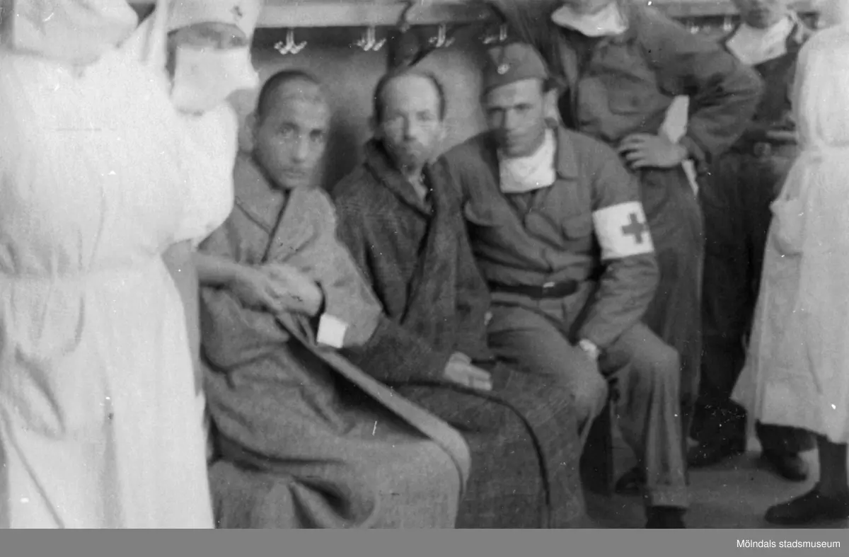 "Karantänsförläggning" på Kvarnbyskolan för överlevande från koncentrationsläger i Tyskland och Polen 1945.  
Skolan fungerade under denna sommar som beredsskapssjukhus.
Sjuksköterskor, flyktingar från koncentrationsläger sitter tillsammans med Röda korsets personal inne i byggnaden.