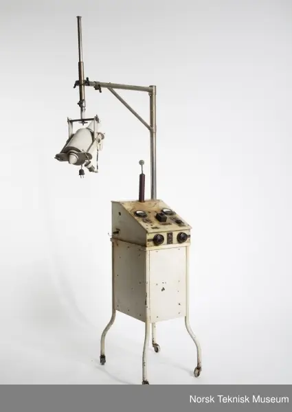 Venstre instrument går til 6 A, antagelig for primærstrømmen til transformatoren. Høyre instrument går til 2 A, antagelig for glødestrøm til røret. Venstre side "Heizanschluss". Høyre side "Heizanschluss für Röhre." Med transformator i oljebeholder og separat hammeravbryter. Vinkelrør med Edison sokkel sitter i trebeholder foret med blygummi og fastspent i svamåegummi. Røret sitter så fast i den stive gummien at det ikke lar seg gjøre å ta den ut.