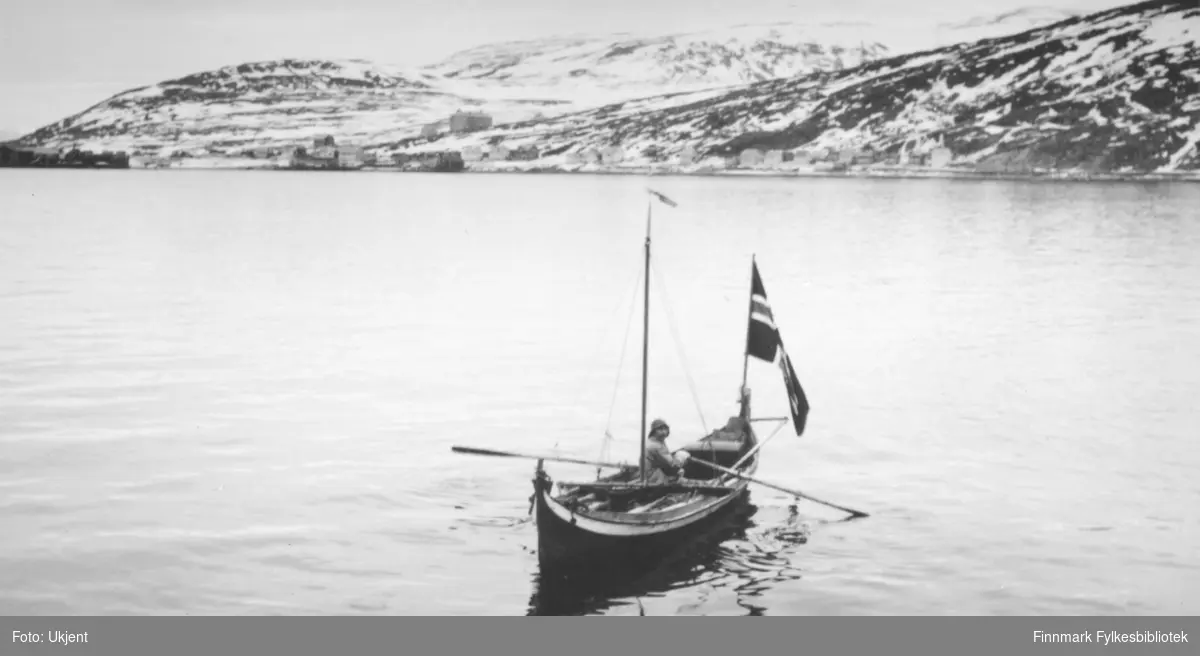 Påsken 1934, 25.mars til 5.april, dro kronprins Olav og kronprinsesse Märtha over Finnmarksvidda med rein og pulk, ledsaget av fylkesmann Hans Gabrielsen, Vadsø. Starten gikk fra Alta, og på Gargia møtte reinskyssen, en raide på 18 rein og tre vappuser. Turen, som tok 12 dager, endte i Vadsø dit følget kom med hest og sleder. Etter at turen var avsluttet dro kongeparet sydover med hurtigruten. Bildet viser en mann i Nordlandsbåt som hilser følget. Foto: ukjent.