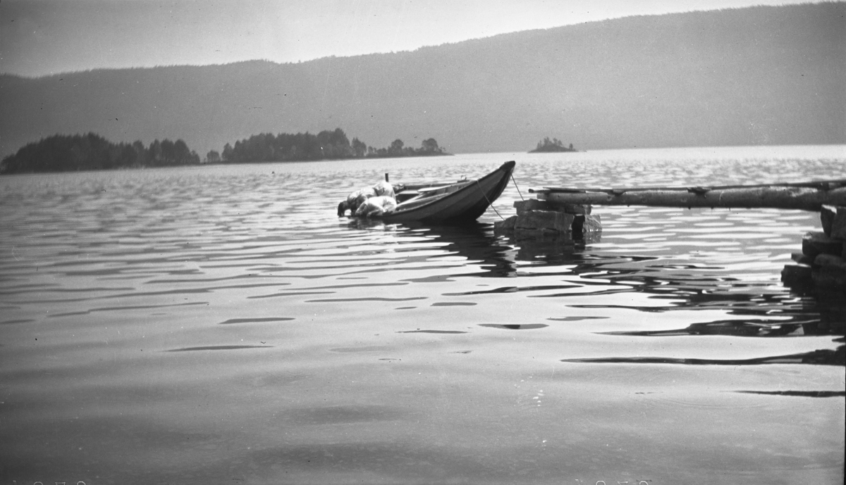 Fotoarkivet etter Gunnar Knudsen. To kvinner ombord i en robåt som dypper sine hoder i fjellvannet/innsjøen.
