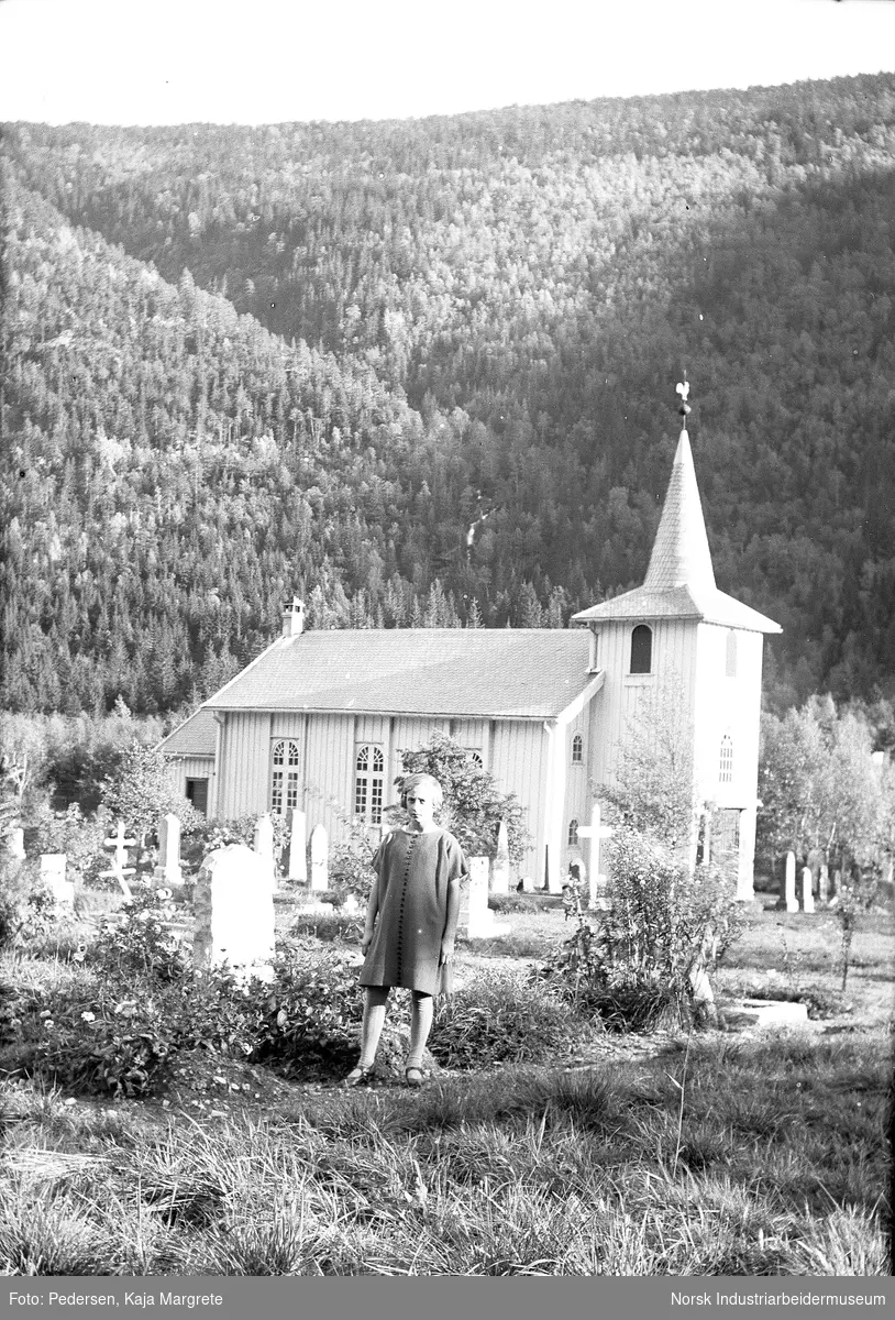 Jente kledd i kortermet kjole stående foran Dal kirke og kirkegård.