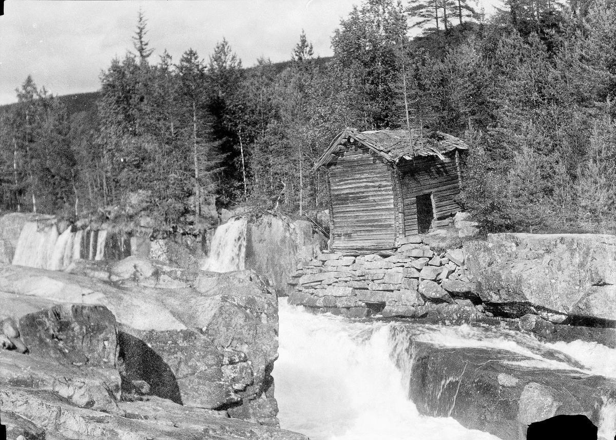 Kvenn (?) ved Austbygdeåi. Laftet bygg står ved elvekanten.