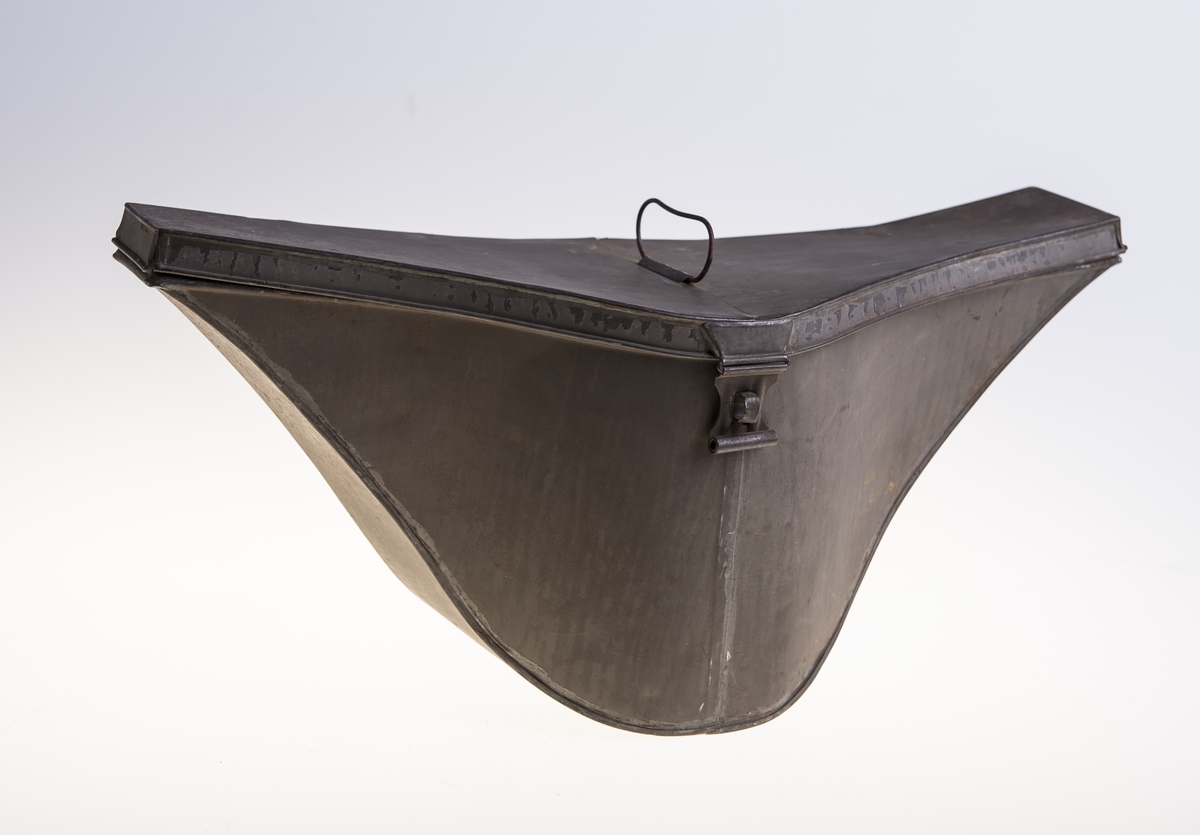 Metall hatteeske med hengslet lokk. Håndtak på lokket og en hempe på siden for hengelås. Esken har ikke fôr.
Hatten i silkefloss, er to snutet med gullbånddekor på hver snute. Langs kanten på den oppbøyde bremmen er det sydd på ripsvevd silkebånd. På den ene siden er det en kokarde med norske farger. Over denne ligger det gullbånd (krampe) festet til en gullfarget knapp med motiv anker. Hatten har fôr og svettebånd med en sløyfe. Det er stempel inne i pullen. To små knapper er sydd fast i pullen Rundt disse er det viklet snor. Hatten har hakebånd med spenne.