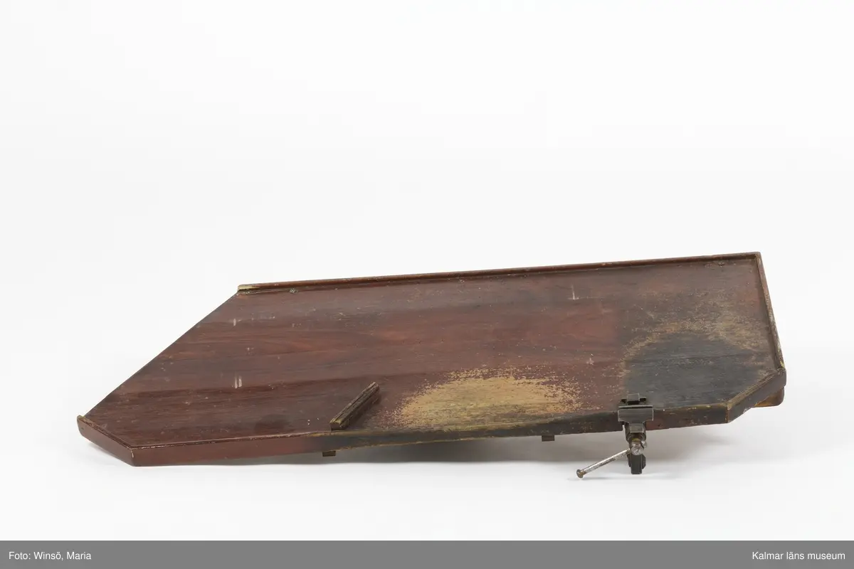 KLM 24993:4:1-6. Arbetsbord, urmakarbord. 6 delar. Möbeln har varit platsbyggd och går ej att montera ihop. Av trä, målad med röd färg. Bordsskiva (:1) med rektangulär form och avfasade kortsidor. På undersidan plats för två utdragslådor. På ovansidan till höger sitter ett skruvstäd av järn fastskruvat. Till bordsskivan finns två lösa ben (:2-:3) som upptill suttit fast på främre delen av skivans undersida, fötterna har varit fastspikade i en vägg. Till bordet hör också ett hyllplan (:4) som suttit under bordsskivan, vilande på benen. Till bordet finns två utdragslådor (:5-:6).