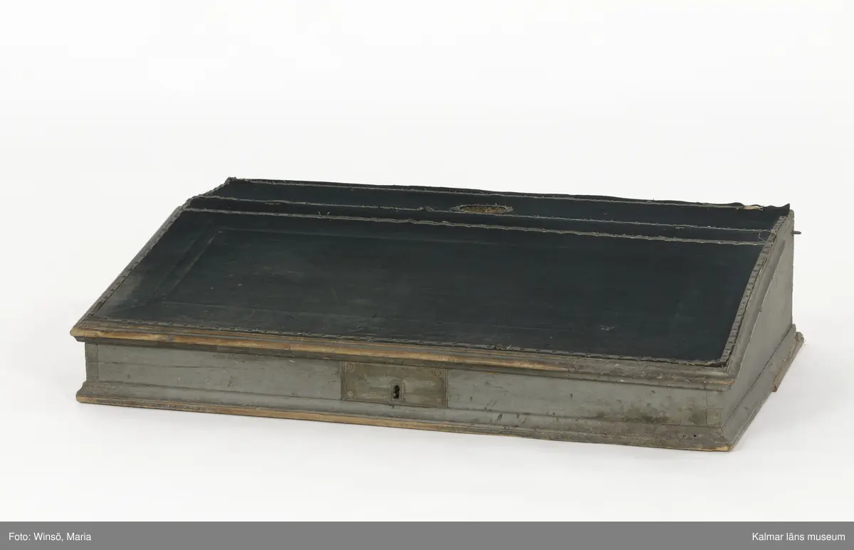 KLM 14272. Pulpet, kontorspulpet. Av trä, är på utsidan målad i grå färg. Baksidan omålad. Snedställt, uppfällbart lock klätt med fastnitat mörkt ylletyg. Nitar av mässing, i nitraderna sitter ett skinnliknande material. På framsidan ett nyckelhål med ett brett beslag av järn. På insidan ett inbyggt lås. Längst upp på pulpeten ett plant utrymme, i mitten ett hål, troligen för bläckhorn. Inuti, längst in, en hylla med fyra fack i två rader. På vänstra utsidan en krok, på den högra en ögla av metall. Har använts tillsammans med pulpet KLM 14273.