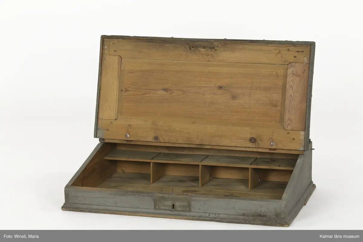 KLM 14272. Pulpet, kontorspulpet. Av trä, är på utsidan målad i grå färg. Baksidan omålad. Snedställt, uppfällbart lock klätt med fastnitat mörkt ylletyg. Nitar av mässing, i nitraderna sitter ett skinnliknande material. På framsidan ett nyckelhål med ett brett beslag av järn. På insidan ett inbyggt lås. Längst upp på pulpeten ett plant utrymme, i mitten ett hål, troligen för bläckhorn. Inuti, längst in, en hylla med fyra fack i två rader. På vänstra utsidan en krok, på den högra en ögla av metall. Har använts tillsammans med pulpet KLM 14273.