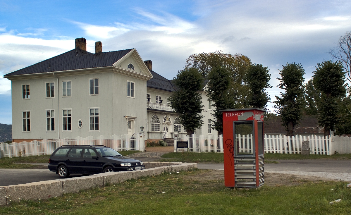 This is the story of how Norway’s most important conversation-space was designed by a young, freshly graduated man from Bergen.

“Norwegian architects are hereby invited…”
In the autumn of 1932, Oslo Telefonanlegginitiated an architectural competition. Finally, Oslo would get its own telephone booth. The city had had so called “talking-stations” from 1885, which in turn were overtaken by automatic telephones 
 only available at selected Narvesen kiosks. The state 
was of the opinion that now was the time to offer the public a better service; public telephone booths open 24/7, like the ones they already had in Sweden and England. But what would they look like, these new telephone booths? What considerations would it
 be necessary to take when designing it? The telegraph board developed a detailed list of demands and restraints: “The booth is intended to be placed outside on the streets and squares and need to be designed so that snow and ice does not hinder the opening and closing of the doors,” they wrote. “To prevent vandalism, theft, uncleanliness etc. inside the booth, it needs to be designed so that from all angles one may see what is going on in there.” Additionally, it would need to withstand storms and bad weather, and “preferably also being whipped by rain mixed with seawater” 

This was not all: The appearance would have to be «pleasing». The booth also needed to be movable, so that it could be taken in to be serviced at Telegrafverket’s main workshops. The reqired material was iron, and the surface was to be spray painted  preferably using car-body paint. There was a requirement for “a writing shelf, a pack shelf, and a suitable place for the telephone catalogue.” Also, there would need to be an illuminated TELEFON  sign, easily visible from all four angles. The total cost for each booth should not exceed 1000 kroner. The first prize for coming up with such a product was 800 kroner.

“Norwegianarchitects are hereby invited to partake in a competition for the design of a telephone booth…”  

The man with the solution
«At some point in 1932, Georg Fredrik sat at a party in Bergen. Maybe he felt a bit lost and forgotten as he often had throughout his life. He retreated to a quiet corner, took out a pencil and strted doodling on a matchbox.  According to my mother, this was how the telephone booth came into being.” In the book “Norges lille røde  historien om telefonkiosken,” Lars Fasting describes his father, the man who is far less known than the iconic architctural structure he left behind. Georg Fredrik Fasting was from Bergen, born into a family of working people and smallholders. One unusual facet of Georg Fredrik was that he was born without ears. His mother made sure he learnt to speak, read and write, 
ut Lars Fasting indicates that his father would seek refuge in drawing when the social challenges became too much to bear. And in the end drawing became his profession. In 1924 he secured a guarantor for a student loan, and started studying to become an a
rchitect at the NTH. Throughout the 1930s he entered several architectural competitions, with drafts produced, according to his son, “after work and in the late hours of the night.”

His efforts were not wasted. Out of 93 entries, with names such as “Flirt”, “Brrr”, “Ring” and “Amor”, the jury selected Fasting’s submission, “RIKS” as the new telephone booth: “The draft shows a strikingly simple solution to the task, technically as well as aesthetically well worked out.”

Taut and provident
Simple and aesthetc are the keywords here. Fasting had designed a booth pointing towards the future, and to modernism. Just how modern it was can be seen by comparing RIKS to the British telephone booth, also designed in the interwar-era. While the British version with it classicistic style is looking back to the heyday of the empire, Fasting’s booth is progressive and functionalistic. Like most Norwegian architects, Fasting broke with the classicistic style of architecture after the Stockholm-exhibition in 1930. “After it, almost all buildings erected in Norway until the German invasion in 1940, were in the functionalistic architectural style,” writes senior curator of architecture at the Norwegian National Museum, Ulf Grønvold, in the book, “Den lille røde”.“TheNorwegian booth is a piece of functionalistic architecture, an asymmetric composition with its roof slab overhanging the word TELEFON, in bold sans seraph lettering,”concludes Ulf Grønvold.

Fashionably red
And it was red. Fasting chose a colour which was part of the modern palette. “A bright red colour, but not as shiny as a signal red, the character of the colour places it among the fashionable colours within functionalism,” states paintings conservator and researcher in NIKU (Norwegian Institute for Cultural Heitage Research), Jon Brænne. In his opinion, Fasting went for visibility without making the booth stand out too much from its surroundings. The original colour was in use up to around 1950, when it changed to signal red. Towards the end of the 1970s the clour was again adjusted towards today’s orangey red.

The design, however, has not changed. RIKS is eighty years and still looks remarkably good. That’s what makes Fasting’s telephone booth a classic  even before it was added to DOCOMOMO’s list over moden icons of design. For Telenor, the telephone booth has served as a pathway into the hearts of the public. For many, Telenor (Televerket) was synonymous with exactly this telephone booth, because this was where one would go to place a call. Having a home
phone was not common until the 1980s. As such the red box became part of the Norwegian everyday and consciousness. The symbol- and publicity value of this is hard to evaluate, but in 2007 it was time to give honour where honour was due, Telenor, in consul
tation with the Directorate for Cultural Heritage, decided to preserve 100 telephone booths for all eternity.

And what about Georg Fredrik Fasting? What happened to him? At the age of 56 an entry in his diary states: «I CAN HEAR». As the first person in th world he had undergone an operation where he had ear canals constructed and eardrums fitted. For the rest of his life, the man behind Norway’s own telephone booth could answer the telephone himself.

Source: Norges lille røde historien om telefonkiosken (2007), issued by The Norwegian Telecom Museum and Telenor Cultural Heritage.