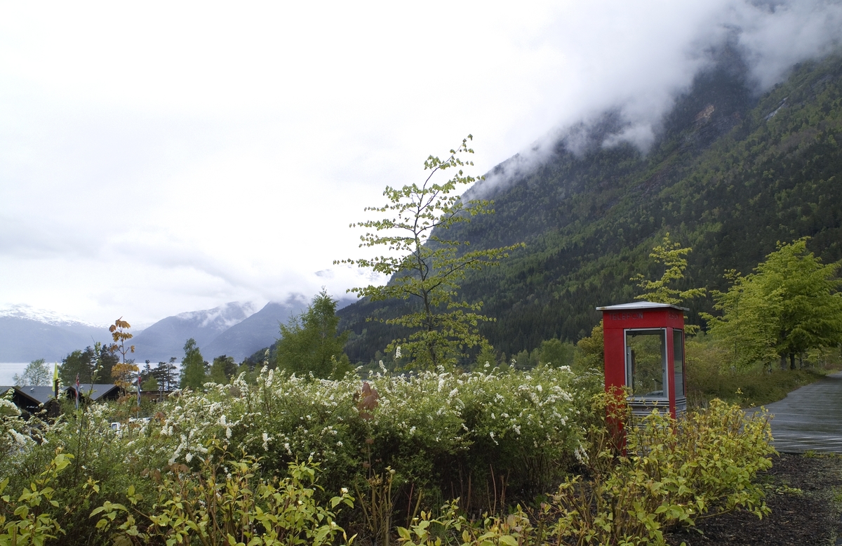 This is the story of how Norway’s most important conversation-space was designed by a young, freshly graduated man from Bergen.

“Norwegian architects are hereby invited…”
In the autumn of 1932, Oslo Telefonanlegginitiated an architectural competition. Finally, Oslo would get its own telephone booth. The city had had so called “talking-stations” from 1885, which in turn were overtaken by automatic telephones 
 only available at selected Narvesen kiosks. The state 
was of the opinion that now was the time to offer the public a better service; public telephone booths open 24/7, like the ones they already had in Sweden and England. But what would they look like, these new telephone booths? What considerations would it
 be necessary to take when designing it? The telegraph board developed a detailed list of demands and restraints: “The booth is intended to be placed outside on the streets and squares and need to be designed so that snow and ice does not hinder the opening and closing of the doors,” they wrote. “To prevent vandalism, theft, uncleanliness etc. inside the booth, it needs to be designed so that from all angles one may see what is going on in there.” Additionally, it would need to withstand storms and bad weather, and “preferably also being whipped by rain mixed with seawater” 

This was not all: The appearance would have to be «pleasing». The booth also needed to be movable, so that it could be taken in to be serviced at Telegrafverket’s main workshops. The reqired material was iron, and the surface was to be spray painted  preferably using car-body paint. There was a requirement for “a writing shelf, a pack shelf, and a suitable place for the telephone catalogue.” Also, there would need to be an illuminated TELEFON  sign, easily visible from all four angles. The total cost for each booth should not exceed 1000 kroner. The first prize for coming up with such a product was 800 kroner.

“Norwegianarchitects are hereby invited to partake in a competition for the design of a telephone booth…”  

The man with the solution
«At some point in 1932, Georg Fredrik sat at a party in Bergen. Maybe he felt a bit lost and forgotten as he often had throughout his life. He retreated to a quiet corner, took out a pencil and strted doodling on a matchbox.  According to my mother, this was how the telephone booth came into being.” In the book “Norges lille røde  historien om telefonkiosken,” Lars Fasting describes his father, the man who is far less known than the iconic architctural structure he left behind. Georg Fredrik Fasting was from Bergen, born into a family of working people and smallholders. One unusual facet of Georg Fredrik was that he was born without ears. His mother made sure he learnt to speak, read and write, 
ut Lars Fasting indicates that his father would seek refuge in drawing when the social challenges became too much to bear. And in the end drawing became his profession. In 1924 he secured a guarantor for a student loan, and started studying to become an a
rchitect at the NTH. Throughout the 1930s he entered several architectural competitions, with drafts produced, according to his son, “after work and in the late hours of the night.”

His efforts were not wasted. Out of 93 entries, with names such as “Flirt”, “Brrr”, “Ring” and “Amor”, the jury selected Fasting’s submission, “RIKS” as the new telephone booth: “The draft shows a strikingly simple solution to the task, technically as well as aesthetically well worked out.”

Taut and provident
Simple and aesthetc are the keywords here. Fasting had designed a booth pointing towards the future, and to modernism. Just how modern it was can be seen by comparing RIKS to the British telephone booth, also designed in the interwar-era. While the British version with it classicistic style is looking back to the heyday of the empire, Fasting’s booth is progressive and functionalistic. Like most Norwegian architects, Fasting broke with the classicistic style of architecture after the Stockholm-exhibition in 1930. “After it, almost all buildings erected in Norway until the German invasion in 1940, were in the functionalistic architectural style,” writes senior curator of architecture at the Norwegian National Museum, Ulf Grønvold, in the book, “Den lille røde”.“TheNorwegian booth is a piece of functionalistic architecture, an asymmetric composition with its roof slab overhanging the word TELEFON, in bold sans seraph lettering,”concludes Ulf Grønvold.

Fashionably red
And it was red. Fasting chose a colour which was part of the modern palette. “A bright red colour, but not as shiny as a signal red, the character of the colour places it among the fashionable colours within functionalism,” states paintings conservator and researcher in NIKU (Norwegian Institute for Cultural Heitage Research), Jon Brænne. In his opinion, Fasting went for visibility without making the booth stand out too much from its surroundings. The original colour was in use up to around 1950, when it changed to signal red. Towards the end of the 1970s the clour was again adjusted towards today’s orangey red.

The design, however, has not changed. RIKS is eighty years and still looks remarkably good. That’s what makes Fasting’s telephone booth a classic  even before it was added to DOCOMOMO’s list over moden icons of design. For Telenor, the telephone booth has served as a pathway into the hearts of the public. For many, Telenor (Televerket) was synonymous with exactly this telephone booth, because this was where one would go to place a call. Having a home
phone was not common until the 1980s. As such the red box became part of the Norwegian everyday and consciousness. The symbol- and publicity value of this is hard to evaluate, but in 2007 it was time to give honour where honour was due, Telenor, in consul
tation with the Directorate for Cultural Heritage, decided to preserve 100 telephone booths for all eternity.

And what about Georg Fredrik Fasting? What happened to him? At the age of 56 an entry in his diary states: «I CAN HEAR». As the first person in th world he had undergone an operation where he had ear canals constructed and eardrums fitted. For the rest of his life, the man behind Norway’s own telephone booth could answer the telephone himself.

Source: Norges lille røde historien om telefonkiosken (2007), issued by The Norwegian Telecom Museum and Telenor Cultural Heritage.