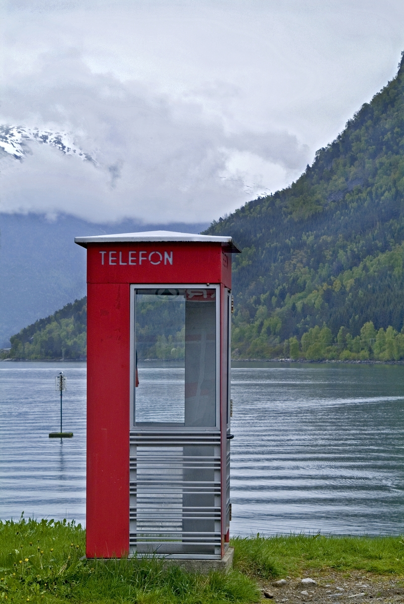 This is the story of how Norway’s most important conversation-space was designed by a young, freshly graduated man from Bergen.

“Norwegian architects are hereby invited…”
In the autumn of 1932, Oslo Telefonanlegginitiated an architectural competition. Finally, Oslo would get its own telephone booth. The city had had so called “talking-stations” from 1885, which in turn were overtaken by automatic telephones 
 only available at selected Narvesen kiosks. The state 
was of the opinion that now was the time to offer the public a better service; public telephone booths open 24/7, like the ones they already had in Sweden and England. But what would they look like, these new telephone booths? What considerations would it
 be necessary to take when designing it? The telegraph board developed a detailed list of demands and restraints: “The booth is intended to be placed outside on the streets and squares and need to be designed so that snow and ice does not hinder the opening and closing of the doors,” they wrote. “To prevent vandalism, theft, uncleanliness etc. inside the booth, it needs to be designed so that from all angles one may see what is going on in there.” Additionally, it would need to withstand storms and bad weather, and “preferably also being whipped by rain mixed with seawater” 

This was not all: The appearance would have to be «pleasing». The booth also needed to be movable, so that it could be taken in to be serviced at Telegrafverket’s main workshops. The reqired material was iron, and the surface was to be spray painted  preferably using car-body paint. There was a requirement for “a writing shelf, a pack shelf, and a suitable place for the telephone catalogue.” Also, there would need to be an illuminated TELEFON  sign, easily visible from all four angles. The total cost for each booth should not exceed 1000 kroner. The first prize for coming up with such a product was 800 kroner.

“Norwegianarchitects are hereby invited to partake in a competition for the design of a telephone booth…”  

The man with the solution
«At some point in 1932, Georg Fredrik sat at a party in Bergen. Maybe he felt a bit lost and forgotten as he often had throughout his life. He retreated to a quiet corner, took out a pencil and strted doodling on a matchbox.  According to my mother, this was how the telephone booth came into being.” In the book “Norges lille røde  historien om telefonkiosken,” Lars Fasting describes his father, the man who is far less known than the iconic architctural structure he left behind. Georg Fredrik Fasting was from Bergen, born into a family of working people and smallholders. One unusual facet of Georg Fredrik was that he was born without ears. His mother made sure he learnt to speak, read and write, 
ut Lars Fasting indicates that his father would seek refuge in drawing when the social challenges became too much to bear. And in the end drawing became his profession. In 1924 he secured a guarantor for a student loan, and started studying to become an a
rchitect at the NTH. Throughout the 1930s he entered several architectural competitions, with drafts produced, according to his son, “after work and in the late hours of the night.”

His efforts were not wasted. Out of 93 entries, with names such as “Flirt”, “Brrr”, “Ring” and “Amor”, the jury selected Fasting’s submission, “RIKS” as the new telephone booth: “The draft shows a strikingly simple solution to the task, technically as well as aesthetically well worked out.”

Taut and provident
Simple and aesthetc are the keywords here. Fasting had designed a booth pointing towards the future, and to modernism. Just how modern it was can be seen by comparing RIKS to the British telephone booth, also designed in the interwar-era. While the British version with it classicistic style is looking back to the heyday of the empire, Fasting’s booth is progressive and functionalistic. Like most Norwegian architects, Fasting broke with the classicistic style of architecture after the Stockholm-exhibition in 1930. “After it, almost all buildings erected in Norway until the German invasion in 1940, were in the functionalistic architectural style,” writes senior curator of architecture at the Norwegian National Museum, Ulf Grønvold, in the book, “Den lille røde”.“TheNorwegian booth is a piece of functionalistic architecture, an asymmetric composition with its roof slab overhanging the word TELEFON, in bold sans seraph lettering,”concludes Ulf Grønvold.

Fashionably red
And it was red. Fasting chose a colour which was part of the modern palette. “A bright red colour, but not as shiny as a signal red, the character of the colour places it among the fashionable colours within functionalism,” states paintings conservator and researcher in NIKU (Norwegian Institute for Cultural Heitage Research), Jon Brænne. In his opinion, Fasting went for visibility without making the booth stand out too much from its surroundings. The original colour was in use up to around 1950, when it changed to signal red. Towards the end of the 1970s the clour was again adjusted towards today’s orangey red.

The design, however, has not changed. RIKS is eighty years and still looks remarkably good. That’s what makes Fasting’s telephone booth a classic  even before it was added to DOCOMOMO’s list over moden icons of design. For Telenor, the telephone booth has served as a pathway into the hearts of the public. For many, Telenor (Televerket) was synonymous with exactly this telephone booth, because this was where one would go to place a call. Having a home
phone was not common until the 1980s. As such the red box became part of the Norwegian everyday and consciousness. The symbol- and publicity value of this is hard to evaluate, but in 2007 it was time to give honour where honour was due, Telenor, in consul
tation with the Directorate for Cultural Heritage, decided to preserve 100 telephone booths for all eternity.

And what about Georg Fredrik Fasting? What happened to him? At the age of 56 an entry in his diary states: «I CAN HEAR». As the first person in th world he had undergone an operation where he had ear canals constructed and eardrums fitted. For the rest of his life, the man behind Norway’s own telephone booth could answer the telephone himself.

Source: Norges lille røde historien om telefonkiosken (2007), issued by The Norwegian Telecom Museum and Telenor Cultural Heritage.