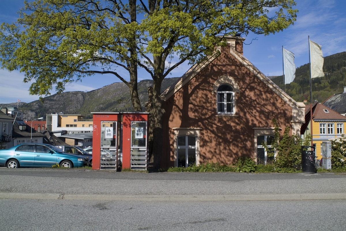 This is the story of how Norway’s most important conversation-space was designed by a young, freshly graduated man from Bergen.

“Norwegian architects are hereby invited…”
In the autumn of 1932, Oslo Telefonanlegginitiated an architectural competition. Finally, Oslo would get its own telephone booth. The city had had so called “talking-stations” from 1885, which in turn were overtaken by automatic telephones 
 only available at selected Narvesen kiosks. The state 
was of the opinion that now was the time to offer the public a better service; public telephone booths open 24/7, like the ones they already had in Sweden and England. But what would they look like, these new telephone booths? What considerations would it
 be necessary to take when designing it? The telegraph board developed a detailed list of demands and restraints: “The booth is intended to be placed outside on the streets and squares and need to be designed so that snow and ice does not hinder the opening and closing of the doors,” they wrote. “To prevent vandalism, theft, uncleanliness etc. inside the booth, it needs to be designed so that from all angles one may see what is going on in there.” Additionally, it would need to withstand storms and bad weather, and “preferably also being whipped by rain mixed with seawater” 

This was not all: The appearance would have to be «pleasing». The booth also needed to be movable, so that it could be taken in to be serviced at Telegrafverket’s main workshops. The reqired material was iron, and the surface was to be spray painted  preferably using car-body paint. There was a requirement for “a writing shelf, a pack shelf, and a suitable place for the telephone catalogue.” Also, there would need to be an illuminated TELEFON  sign, easily visible from all four angles. The total cost for each booth should not exceed 1000 kroner. The first prize for coming up with such a product was 800 kroner.

“Norwegianarchitects are hereby invited to partake in a competition for the design of a telephone booth…”  

The man with the solution
«At some point in 1932, Georg Fredrik sat at a party in Bergen. Maybe he felt a bit lost and forgotten as he often had throughout his life. He retreated to a quiet corner, took out a pencil and strted doodling on a matchbox.  According to my mother, this was how the telephone booth came into being.” In the book “Norges lille røde  historien om telefonkiosken,” Lars Fasting describes his father, the man who is far less known than the iconic architctural structure he left behind. Georg Fredrik Fasting was from Bergen, born into a family of working people and smallholders. One unusual facet of Georg Fredrik was that he was born without ears. His mother made sure he learnt to speak, read and write, 
ut Lars Fasting indicates that his father would seek refuge in drawing when the social challenges became too much to bear. And in the end drawing became his profession. In 1924 he secured a guarantor for a student loan, and started studying to become an a
rchitect at the NTH. Throughout the 1930s he entered several architectural competitions, with drafts produced, according to his son, “after work and in the late hours of the night.”

His efforts were not wasted. Out of 93 entries, with names such as “Flirt”, “Brrr”, “Ring” and “Amor”, the jury selected Fasting’s submission, “RIKS” as the new telephone booth: “The draft shows a strikingly simple solution to the task, technically as well as aesthetically well worked out.”

Taut and provident
Simple and aesthetc are the keywords here. Fasting had designed a booth pointing towards the future, and to modernism. Just how modern it was can be seen by comparing RIKS to the British telephone booth, also designed in the interwar-era. While the British version with it classicistic style is looking back to the heyday of the empire, Fasting’s booth is progressive and functionalistic. Like most Norwegian architects, Fasting broke with the classicistic style of architecture after the Stockholm-exhibition in 1930. “After it, almost all buildings erected in Norway until the German invasion in 1940, were in the functionalistic architectural style,” writes senior curator of architecture at the Norwegian National Museum, Ulf Grønvold, in the book, “Den lille røde”.“TheNorwegian booth is a piece of functionalistic architecture, an asymmetric composition with its roof slab overhanging the word TELEFON, in bold sans seraph lettering,”concludes Ulf Grønvold.

Fashionably red
And it was red. Fasting chose a colour which was part of the modern palette. “A bright red colour, but not as shiny as a signal red, the character of the colour places it among the fashionable colours within functionalism,” states paintings conservator and researcher in NIKU (Norwegian Institute for Cultural Heitage Research), Jon Brænne. In his opinion, Fasting went for visibility without making the booth stand out too much from its surroundings. The original colour was in use up to around 1950, when it changed to signal red. Towards the end of the 1970s the clour was again adjusted towards today’s orangey red.

The design, however, has not changed. RIKS is eighty years and still looks remarkably good. That’s what makes Fasting’s telephone booth a classic  even before it was added to DOCOMOMO’s list over moden icons of design. For Telenor, the telephone booth has served as a pathway into the hearts of the public. For many, Telenor (Televerket) was synonymous with exactly this telephone booth, because this was where one would go to place a call. Having a home
phone was not common until the 1980s. As such the red box became part of the Norwegian everyday and consciousness. The symbol- and publicity value of this is hard to evaluate, but in 2007 it was time to give honour where honour was due, Telenor, in consul
tation with the Directorate for Cultural Heritage, decided to preserve 100 telephone booths for all eternity.

And what about Georg Fredrik Fasting? What happened to him? At the age of 56 an entry in his diary states: «I CAN HEAR». As the first person in th world he had undergone an operation where he had ear canals constructed and eardrums fitted. For the rest of his life, the man behind Norway’s own telephone booth could answer the telephone himself.

Source: Norges lille røde historien om telefonkiosken (2007), issued by The Norwegian Telecom Museum and Telenor Cultural Heritage.