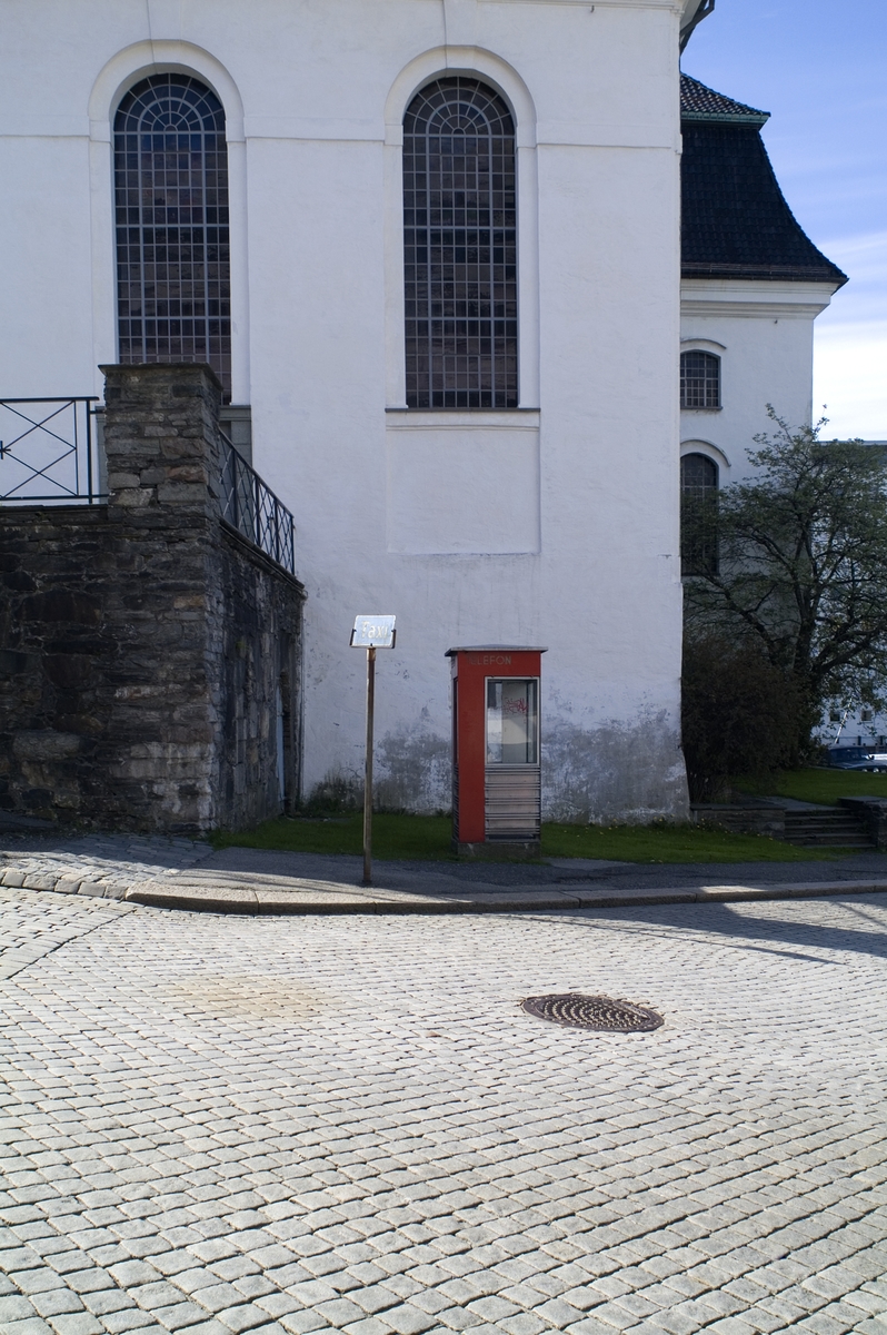 This is the story of how Norway’s most important conversation-space was designed by a young, freshly graduated man from Bergen.

“Norwegian architects are hereby invited…”
In the autumn of 1932, Oslo Telefonanlegginitiated an architectural competition. Finally, Oslo would get its own telephone booth. The city had had so called “talking-stations” from 1885, which in turn were overtaken by automatic telephones 
 only available at selected Narvesen kiosks. The state 
was of the opinion that now was the time to offer the public a better service; public telephone booths open 24/7, like the ones they already had in Sweden and England. But what would they look like, these new telephone booths? What considerations would it
 be necessary to take when designing it? The telegraph board developed a detailed list of demands and restraints: “The booth is intended to be placed outside on the streets and squares and need to be designed so that snow and ice does not hinder the opening and closing of the doors,” they wrote. “To prevent vandalism, theft, uncleanliness etc. inside the booth, it needs to be designed so that from all angles one may see what is going on in there.” Additionally, it would need to withstand storms and bad weather, and “preferably also being whipped by rain mixed with seawater” 

This was not all: The appearance would have to be «pleasing». The booth also needed to be movable, so that it could be taken in to be serviced at Telegrafverket’s main workshops. The reqired material was iron, and the surface was to be spray painted  preferably using car-body paint. There was a requirement for “a writing shelf, a pack shelf, and a suitable place for the telephone catalogue.” Also, there would need to be an illuminated TELEFON  sign, easily visible from all four angles. The total cost for each booth should not exceed 1000 kroner. The first prize for coming up with such a product was 800 kroner.

“Norwegianarchitects are hereby invited to partake in a competition for the design of a telephone booth…”  

The man with the solution
«At some point in 1932, Georg Fredrik sat at a party in Bergen. Maybe he felt a bit lost and forgotten as he often had throughout his life. He retreated to a quiet corner, took out a pencil and strted doodling on a matchbox.  According to my mother, this was how the telephone booth came into being.” In the book “Norges lille røde  historien om telefonkiosken,” Lars Fasting describes his father, the man who is far less known than the iconic architctural structure he left behind. Georg Fredrik Fasting was from Bergen, born into a family of working people and smallholders. One unusual facet of Georg Fredrik was that he was born without ears. His mother made sure he learnt to speak, read and write, 
ut Lars Fasting indicates that his father would seek refuge in drawing when the social challenges became too much to bear. And in the end drawing became his profession. In 1924 he secured a guarantor for a student loan, and started studying to become an a
rchitect at the NTH. Throughout the 1930s he entered several architectural competitions, with drafts produced, according to his son, “after work and in the late hours of the night.”

His efforts were not wasted. Out of 93 entries, with names such as “Flirt”, “Brrr”, “Ring” and “Amor”, the jury selected Fasting’s submission, “RIKS” as the new telephone booth: “The draft shows a strikingly simple solution to the task, technically as well as aesthetically well worked out.”

Taut and provident
Simple and aesthetc are the keywords here. Fasting had designed a booth pointing towards the future, and to modernism. Just how modern it was can be seen by comparing RIKS to the British telephone booth, also designed in the interwar-era. While the British version with it classicistic style is looking back to the heyday of the empire, Fasting’s booth is progressive and functionalistic. Like most Norwegian architects, Fasting broke with the classicistic style of architecture after the Stockholm-exhibition in 1930. “After it, almost all buildings erected in Norway until the German invasion in 1940, were in the functionalistic architectural style,” writes senior curator of architecture at the Norwegian National Museum, Ulf Grønvold, in the book, “Den lille røde”.“TheNorwegian booth is a piece of functionalistic architecture, an asymmetric composition with its roof slab overhanging the word TELEFON, in bold sans seraph lettering,”concludes Ulf Grønvold.

Fashionably red
And it was red. Fasting chose a colour which was part of the modern palette. “A bright red colour, but not as shiny as a signal red, the character of the colour places it among the fashionable colours within functionalism,” states paintings conservator and researcher in NIKU (Norwegian Institute for Cultural Heitage Research), Jon Brænne. In his opinion, Fasting went for visibility without making the booth stand out too much from its surroundings. The original colour was in use up to around 1950, when it changed to signal red. Towards the end of the 1970s the clour was again adjusted towards today’s orangey red.

The design, however, has not changed. RIKS is eighty years and still looks remarkably good. That’s what makes Fasting’s telephone booth a classic  even before it was added to DOCOMOMO’s list over moden icons of design. For Telenor, the telephone booth has served as a pathway into the hearts of the public. For many, Telenor (Televerket) was synonymous with exactly this telephone booth, because this was where one would go to place a call. Having a home
phone was not common until the 1980s. As such the red box became part of the Norwegian everyday and consciousness. The symbol- and publicity value of this is hard to evaluate, but in 2007 it was time to give honour where honour was due, Telenor, in consul
tation with the Directorate for Cultural Heritage, decided to preserve 100 telephone booths for all eternity.

And what about Georg Fredrik Fasting? What happened to him? At the age of 56 an entry in his diary states: «I CAN HEAR». As the first person in th world he had undergone an operation where he had ear canals constructed and eardrums fitted. For the rest of his life, the man behind Norway’s own telephone booth could answer the telephone himself.

Source: Norges lille røde historien om telefonkiosken (2007), issued by The Norwegian Telecom Museum and Telenor Cultural Heritage.
