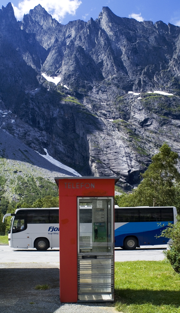 This is the story of how Norway’s most important conversation-space was designed by a young, freshly graduated man from Bergen.

“Norwegian architects are hereby invited…”
In the autumn of 1932, Oslo Telefonanlegginitiated an architectural competition. Finally, Oslo would get its own telephone booth. The city had had so called “talking-stations” from 1885, which in turn were overtaken by automatic telephones 
 only available at selected Narvesen kiosks. The state 
was of the opinion that now was the time to offer the public a better service; public telephone booths open 24/7, like the ones they already had in Sweden and England. But what would they look like, these new telephone booths? What considerations would it
 be necessary to take when designing it? The telegraph board developed a detailed list of demands and restraints: “The booth is intended to be placed outside on the streets and squares and need to be designed so that snow and ice does not hinder the opening and closing of the doors,” they wrote. “To prevent vandalism, theft, uncleanliness etc. inside the booth, it needs to be designed so that from all angles one may see what is going on in there.” Additionally, it would need to withstand storms and bad weather, and “preferably also being whipped by rain mixed with seawater” 

This was not all: The appearance would have to be «pleasing». The booth also needed to be movable, so that it could be taken in to be serviced at Telegrafverket’s main workshops. The reqired material was iron, and the surface was to be spray painted  preferably using car-body paint. There was a requirement for “a writing shelf, a pack shelf, and a suitable place for the telephone catalogue.” Also, there would need to be an illuminated TELEFON  sign, easily visible from all four angles. The total cost for each booth should not exceed 1000 kroner. The first prize for coming up with such a product was 800 kroner.

“Norwegianarchitects are hereby invited to partake in a competition for the design of a telephone booth…”  

The man with the solution
«At some point in 1932, Georg Fredrik sat at a party in Bergen. Maybe he felt a bit lost and forgotten as he often had throughout his life. He retreated to a quiet corner, took out a pencil and strted doodling on a matchbox.  According to my mother, this was how the telephone booth came into being.” In the book “Norges lille røde  historien om telefonkiosken,” Lars Fasting describes his father, the man who is far less known than the iconic architctural structure he left behind. Georg Fredrik Fasting was from Bergen, born into a family of working people and smallholders. One unusual facet of Georg Fredrik was that he was born without ears. His mother made sure he learnt to speak, read and write, 
ut Lars Fasting indicates that his father would seek refuge in drawing when the social challenges became too much to bear. And in the end drawing became his profession. In 1924 he secured a guarantor for a student loan, and started studying to become an a
rchitect at the NTH. Throughout the 1930s he entered several architectural competitions, with drafts produced, according to his son, “after work and in the late hours of the night.”

His efforts were not wasted. Out of 93 entries, with names such as “Flirt”, “Brrr”, “Ring” and “Amor”, the jury selected Fasting’s submission, “RIKS” as the new telephone booth: “The draft shows a strikingly simple solution to the task, technically as well as aesthetically well worked out.”

Taut and provident
Simple and aesthetc are the keywords here. Fasting had designed a booth pointing towards the future, and to modernism. Just how modern it was can be seen by comparing RIKS to the British telephone booth, also designed in the interwar-era. While the British version with it classicistic style is looking back to the heyday of the empire, Fasting’s booth is progressive and functionalistic. Like most Norwegian architects, Fasting broke with the classicistic style of architecture after the Stockholm-exhibition in 1930. “After it, almost all buildings erected in Norway until the German invasion in 1940, were in the functionalistic architectural style,” writes senior curator of architecture at the Norwegian National Museum, Ulf Grønvold, in the book, “Den lille røde”.“TheNorwegian booth is a piece of functionalistic architecture, an asymmetric composition with its roof slab overhanging the word TELEFON, in bold sans seraph lettering,”concludes Ulf Grønvold.

Fashionably red
And it was red. Fasting chose a colour which was part of the modern palette. “A bright red colour, but not as shiny as a signal red, the character of the colour places it among the fashionable colours within functionalism,” states paintings conservator and researcher in NIKU (Norwegian Institute for Cultural Heitage Research), Jon Brænne. In his opinion, Fasting went for visibility without making the booth stand out too much from its surroundings. The original colour was in use up to around 1950, when it changed to signal red. Towards the end of the 1970s the clour was again adjusted towards today’s orangey red.

The design, however, has not changed. RIKS is eighty years and still looks remarkably good. That’s what makes Fasting’s telephone booth a classic  even before it was added to DOCOMOMO’s list over moden icons of design. For Telenor, the telephone booth has served as a pathway into the hearts of the public. For many, Telenor (Televerket) was synonymous with exactly this telephone booth, because this was where one would go to place a call. Having a home
phone was not common until the 1980s. As such the red box became part of the Norwegian everyday and consciousness. The symbol- and publicity value of this is hard to evaluate, but in 2007 it was time to give honour where honour was due, Telenor, in consul
tation with the Directorate for Cultural Heritage, decided to preserve 100 telephone booths for all eternity.

And what about Georg Fredrik Fasting? What happened to him? At the age of 56 an entry in his diary states: «I CAN HEAR». As the first person in th world he had undergone an operation where he had ear canals constructed and eardrums fitted. For the rest of his life, the man behind Norway’s own telephone booth could answer the telephone himself.

Source: Norges lille røde historien om telefonkiosken (2007), issued by The Norwegian Telecom Museum and Telenor Cultural Heritage.