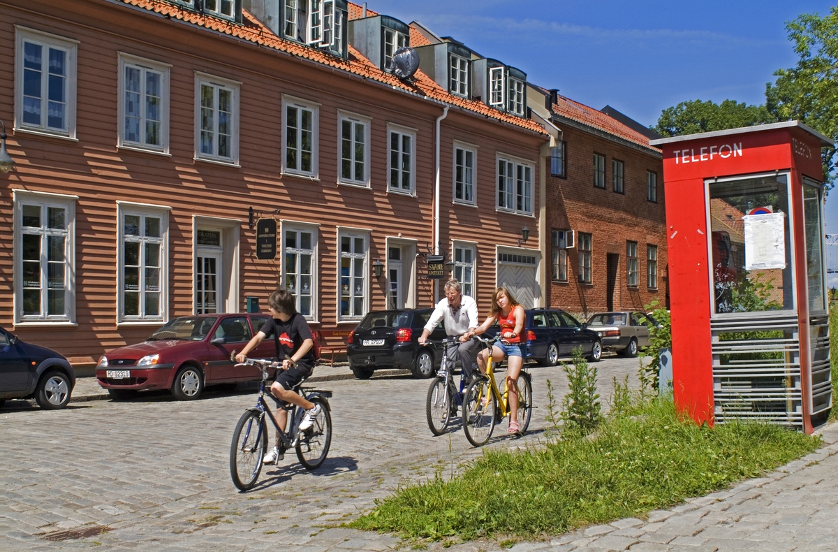 This is the story of how Norway’s most important conversation-space was designed by a young, freshly graduated man from Bergen.

“Norwegian architects are hereby invited…”
In the autumn of 1932, Oslo Telefonanlegginitiated an architectural competition. Finally, Oslo would get its own telephone booth. The city had had so called “talking-stations” from 1885, which in turn were overtaken by automatic telephones 
 only available at selected Narvesen kiosks. The state 
was of the opinion that now was the time to offer the public a better service; public telephone booths open 24/7, like the ones they already had in Sweden and England. But what would they look like, these new telephone booths? What considerations would it
 be necessary to take when designing it? The telegraph board developed a detailed list of demands and restraints: “The booth is intended to be placed outside on the streets and squares and need to be designed so that snow and ice does not hinder the opening and closing of the doors,” they wrote. “To prevent vandalism, theft, uncleanliness etc. inside the booth, it needs to be designed so that from all angles one may see what is going on in there.” Additionally, it would need to withstand storms and bad weather, and “preferably also being whipped by rain mixed with seawater” 

This was not all: The appearance would have to be «pleasing». The booth also needed to be movable, so that it could be taken in to be serviced at Telegrafverket’s main workshops. The reqired material was iron, and the surface was to be spray painted  preferably using car-body paint. There was a requirement for “a writing shelf, a pack shelf, and a suitable place for the telephone catalogue.” Also, there would need to be an illuminated TELEFON  sign, easily visible from all four angles. The total cost for each booth should not exceed 1000 kroner. The first prize for coming up with such a product was 800 kroner.

“Norwegianarchitects are hereby invited to partake in a competition for the design of a telephone booth…”  

The man with the solution
«At some point in 1932, Georg Fredrik sat at a party in Bergen. Maybe he felt a bit lost and forgotten as he often had throughout his life. He retreated to a quiet corner, took out a pencil and strted doodling on a matchbox.  According to my mother, this was how the telephone booth came into being.” In the book “Norges lille røde  historien om telefonkiosken,” Lars Fasting describes his father, the man who is far less known than the iconic architctural structure he left behind. Georg Fredrik Fasting was from Bergen, born into a family of working people and smallholders. One unusual facet of Georg Fredrik was that he was born without ears. His mother made sure he learnt to speak, read and write, 
ut Lars Fasting indicates that his father would seek refuge in drawing when the social challenges became too much to bear. And in the end drawing became his profession. In 1924 he secured a guarantor for a student loan, and started studying to become an a
rchitect at the NTH. Throughout the 1930s he entered several architectural competitions, with drafts produced, according to his son, “after work and in the late hours of the night.”

His efforts were not wasted. Out of 93 entries, with names such as “Flirt”, “Brrr”, “Ring” and “Amor”, the jury selected Fasting’s submission, “RIKS” as the new telephone booth: “The draft shows a strikingly simple solution to the task, technically as well as aesthetically well worked out.”

Taut and provident
Simple and aesthetc are the keywords here. Fasting had designed a booth pointing towards the future, and to modernism. Just how modern it was can be seen by comparing RIKS to the British telephone booth, also designed in the interwar-era. While the British version with it classicistic style is looking back to the heyday of the empire, Fasting’s booth is progressive and functionalistic. Like most Norwegian architects, Fasting broke with the classicistic style of architecture after the Stockholm-exhibition in 1930. “After it, almost all buildings erected in Norway until the German invasion in 1940, were in the functionalistic architectural style,” writes senior curator of architecture at the Norwegian National Museum, Ulf Grønvold, in the book, “Den lille røde”.“TheNorwegian booth is a piece of functionalistic architecture, an asymmetric composition with its roof slab overhanging the word TELEFON, in bold sans seraph lettering,”concludes Ulf Grønvold.

Fashionably red
And it was red. Fasting chose a colour which was part of the modern palette. “A bright red colour, but not as shiny as a signal red, the character of the colour places it among the fashionable colours within functionalism,” states paintings conservator and researcher in NIKU (Norwegian Institute for Cultural Heitage Research), Jon Brænne. In his opinion, Fasting went for visibility without making the booth stand out too much from its surroundings. The original colour was in use up to around 1950, when it changed to signal red. Towards the end of the 1970s the clour was again adjusted towards today’s orangey red.

The design, however, has not changed. RIKS is eighty years and still looks remarkably good. That’s what makes Fasting’s telephone booth a classic  even before it was added to DOCOMOMO’s list over moden icons of design. For Telenor, the telephone booth has served as a pathway into the hearts of the public. For many, Telenor (Televerket) was synonymous with exactly this telephone booth, because this was where one would go to place a call. Having a home
phone was not common until the 1980s. As such the red box became part of the Norwegian everyday and consciousness. The symbol- and publicity value of this is hard to evaluate, but in 2007 it was time to give honour where honour was due, Telenor, in consul
tation with the Directorate for Cultural Heritage, decided to preserve 100 telephone booths for all eternity.

And what about Georg Fredrik Fasting? What happened to him? At the age of 56 an entry in his diary states: «I CAN HEAR». As the first person in th world he had undergone an operation where he had ear canals constructed and eardrums fitted. For the rest of his life, the man behind Norway’s own telephone booth could answer the telephone himself.

Source: Norges lille røde historien om telefonkiosken (2007), issued by The Norwegian Telecom Museum and Telenor Cultural Heritage.