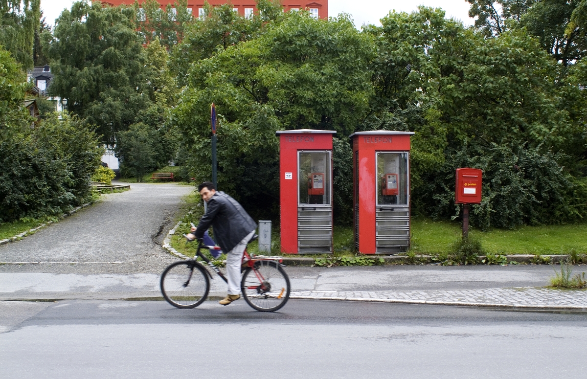 This is the story of how Norway’s most important conversation-space was designed by a young, freshly graduated man from Bergen.

“Norwegian architects are hereby invited…”
In the autumn of 1932, Oslo Telefonanlegginitiated an architectural competition. Finally, Oslo would get its own telephone booth. The city had had so called “talking-stations” from 1885, which in turn were overtaken by automatic telephones 
 only available at selected Narvesen kiosks. The state 
was of the opinion that now was the time to offer the public a better service; public telephone booths open 24/7, like the ones they already had in Sweden and England. But what would they look like, these new telephone booths? What considerations would it
 be necessary to take when designing it? The telegraph board developed a detailed list of demands and restraints: “The booth is intended to be placed outside on the streets and squares and need to be designed so that snow and ice does not hinder the opening and closing of the doors,” they wrote. “To prevent vandalism, theft, uncleanliness etc. inside the booth, it needs to be designed so that from all angles one may see what is going on in there.” Additionally, it would need to withstand storms and bad weather, and “preferably also being whipped by rain mixed with seawater” 

This was not all: The appearance would have to be «pleasing». The booth also needed to be movable, so that it could be taken in to be serviced at Telegrafverket’s main workshops. The reqired material was iron, and the surface was to be spray painted  preferably using car-body paint. There was a requirement for “a writing shelf, a pack shelf, and a suitable place for the telephone catalogue.” Also, there would need to be an illuminated TELEFON  sign, easily visible from all four angles. The total cost for each booth should not exceed 1000 kroner. The first prize for coming up with such a product was 800 kroner.

“Norwegianarchitects are hereby invited to partake in a competition for the design of a telephone booth…”  

The man with the solution
«At some point in 1932, Georg Fredrik sat at a party in Bergen. Maybe he felt a bit lost and forgotten as he often had throughout his life. He retreated to a quiet corner, took out a pencil and strted doodling on a matchbox.  According to my mother, this was how the telephone booth came into being.” In the book “Norges lille røde  historien om telefonkiosken,” Lars Fasting describes his father, the man who is far less known than the iconic architctural structure he left behind. Georg Fredrik Fasting was from Bergen, born into a family of working people and smallholders. One unusual facet of Georg Fredrik was that he was born without ears. His mother made sure he learnt to speak, read and write, 
ut Lars Fasting indicates that his father would seek refuge in drawing when the social challenges became too much to bear. And in the end drawing became his profession. In 1924 he secured a guarantor for a student loan, and started studying to become an a
rchitect at the NTH. Throughout the 1930s he entered several architectural competitions, with drafts produced, according to his son, “after work and in the late hours of the night.”

His efforts were not wasted. Out of 93 entries, with names such as “Flirt”, “Brrr”, “Ring” and “Amor”, the jury selected Fasting’s submission, “RIKS” as the new telephone booth: “The draft shows a strikingly simple solution to the task, technically as well as aesthetically well worked out.”

Taut and provident
Simple and aesthetc are the keywords here. Fasting had designed a booth pointing towards the future, and to modernism. Just how modern it was can be seen by comparing RIKS to the British telephone booth, also designed in the interwar-era. While the British version with it classicistic style is looking back to the heyday of the empire, Fasting’s booth is progressive and functionalistic. Like most Norwegian architects, Fasting broke with the classicistic style of architecture after the Stockholm-exhibition in 1930. “After it, almost all buildings erected in Norway until the German invasion in 1940, were in the functionalistic architectural style,” writes senior curator of architecture at the Norwegian National Museum, Ulf Grønvold, in the book, “Den lille røde”.“TheNorwegian booth is a piece of functionalistic architecture, an asymmetric composition with its roof slab overhanging the word TELEFON, in bold sans seraph lettering,”concludes Ulf Grønvold.

Fashionably red
And it was red. Fasting chose a colour which was part of the modern palette. “A bright red colour, but not as shiny as a signal red, the character of the colour places it among the fashionable colours within functionalism,” states paintings conservator and researcher in NIKU (Norwegian Institute for Cultural Heitage Research), Jon Brænne. In his opinion, Fasting went for visibility without making the booth stand out too much from its surroundings. The original colour was in use up to around 1950, when it changed to signal red. Towards the end of the 1970s the clour was again adjusted towards today’s orangey red.

The design, however, has not changed. RIKS is eighty years and still looks remarkably good. That’s what makes Fasting’s telephone booth a classic  even before it was added to DOCOMOMO’s list over moden icons of design. For Telenor, the telephone booth has served as a pathway into the hearts of the public. For many, Telenor (Televerket) was synonymous with exactly this telephone booth, because this was where one would go to place a call. Having a home
phone was not common until the 1980s. As such the red box became part of the Norwegian everyday and consciousness. The symbol- and publicity value of this is hard to evaluate, but in 2007 it was time to give honour where honour was due, Telenor, in consul
tation with the Directorate for Cultural Heritage, decided to preserve 100 telephone booths for all eternity.

And what about Georg Fredrik Fasting? What happened to him? At the age of 56 an entry in his diary states: «I CAN HEAR». As the first person in th world he had undergone an operation where he had ear canals constructed and eardrums fitted. For the rest of his life, the man behind Norway’s own telephone booth could answer the telephone himself.

Source: Norges lille røde historien om telefonkiosken (2007), issued by The Norwegian Telecom Museum and Telenor Cultural Heritage.