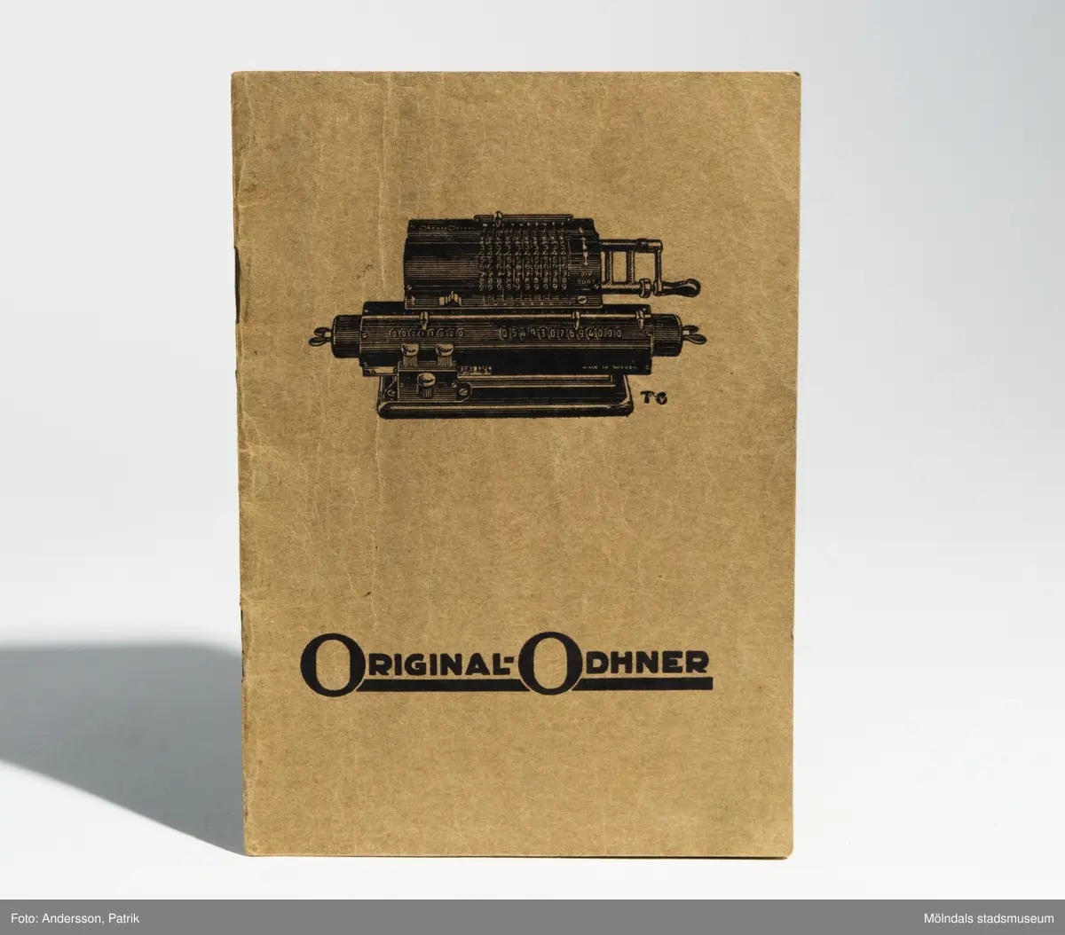 Räknesnurran: Original-Odhner Arithmos Typ 5, tillverkad av Aktiebolaget Original-Odhner i Göteborg mellan 1919 - 1922.Texten: "AKTIEBOLAGET ORIGINAL-ODHNER GÖTEBORG   Arithmos SVERIGE INREG. VARUMÄRKE  TYP 5   MADE IN SWEDEN", finns gjutet i räknesnurran.Vet inte av vem eller i vilket sammanhang räknesnurran har användts. Givare Eva-Lis Sundström från Kållered.Original-Odhner var en svensk tillverkare och ett varumärke som tillverkade den så kallade räknesnurran. Företaget var verksamt i Sverige 1918 - 1972. Det var svensken Willgodt Odhner som uppfann räknesnurran, en apparat som kunde hantera alla de fyra räknesätten.Principen med den nya uppfinningen är att räknesnurran har ett system av så kallade pinnhjul med ett föränderligt antal kuggar. Genom inställningsarmar regleras antalet kuggar som är i funktion. Uppfinningen togs sedan efter av flera andra tillverkare. W. Odhners räknesnurra fick därför namnet Original-Odhner, för att kunna hålla isär från kopiorna.Svensken W. Odhners öppnade först två fabriker i Sant Petersburg mellan 1886-1894. När han dog i september 1905 övertogs företaget av sonen Alexander Hj. Odhner (1873-1918) och svärsonen Karl Siewert. 1912 ombildades Original-Odhner till ett familjeföretag. Några år senare lyckades man flytta tillverkningen till Sverige.Det var A. Odhners sysslingar, bröderna Sven och Erik Wingquist från SKF som tog familjeföretaget Original-Odhner till Göteborg.  Den 1 februari 1918 skrevs kontraktet under, av E. Wingquist, A. Odhner och K. Siewert och Original-Odhner slog upp sina portar.MåttLängd: 195 mm, Bredd: 255 mm Höjd: 140 mm