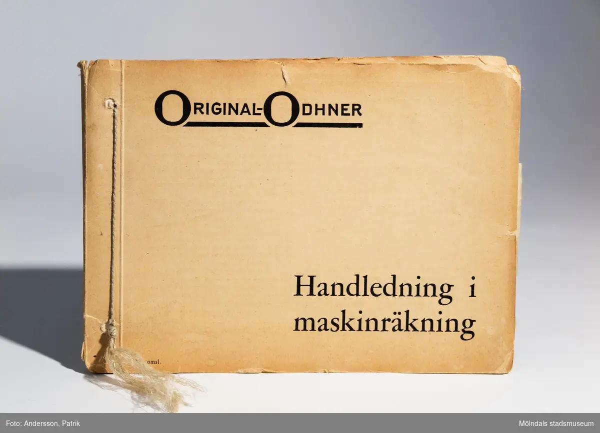 Räknesnurran: Original-Odhner Arithmos Typ 5, tillverkad av Aktiebolaget Original-Odhner i Göteborg mellan 1919 - 1922.Texten: "AKTIEBOLAGET ORIGINAL-ODHNER GÖTEBORG   Arithmos SVERIGE INREG. VARUMÄRKE  TYP 5   MADE IN SWEDEN", finns gjutet i räknesnurran.Vet inte av vem eller i vilket sammanhang räknesnurran har användts. Givare Eva-Lis Sundström från Kållered.Original-Odhner var en svensk tillverkare och ett varumärke som tillverkade den så kallade räknesnurran. Företaget var verksamt i Sverige 1918 - 1972. Det var svensken Willgodt Odhner som uppfann räknesnurran, en apparat som kunde hantera alla de fyra räknesätten.Principen med den nya uppfinningen är att räknesnurran har ett system av så kallade pinnhjul med ett föränderligt antal kuggar. Genom inställningsarmar regleras antalet kuggar som är i funktion. Uppfinningen togs sedan efter av flera andra tillverkare. W. Odhners räknesnurra fick därför namnet Original-Odhner, för att kunna hålla isär från kopiorna.Svensken W. Odhners öppnade först två fabriker i Sant Petersburg mellan 1886-1894. När han dog i september 1905 övertogs företaget av sonen Alexander Hj. Odhner (1873-1918) och svärsonen Karl Siewert. 1912 ombildades Original-Odhner till ett familjeföretag. Några år senare lyckades man flytta tillverkningen till Sverige.Det var A. Odhners sysslingar, bröderna Sven och Erik Wingquist från SKF som tog familjeföretaget Original-Odhner till Göteborg.  Den 1 februari 1918 skrevs kontraktet under, av E. Wingquist, A. Odhner och K. Siewert och Original-Odhner slog upp sina portar.MåttLängd: 195 mm, Bredd: 255 mm Höjd: 140 mm