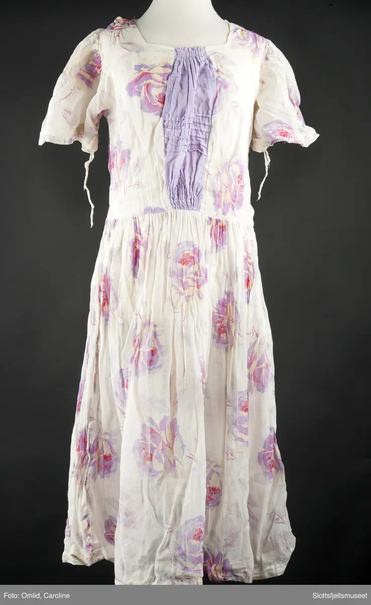 Hvit med lilla blomster. Omsydd under krigen. Trykknapper bak