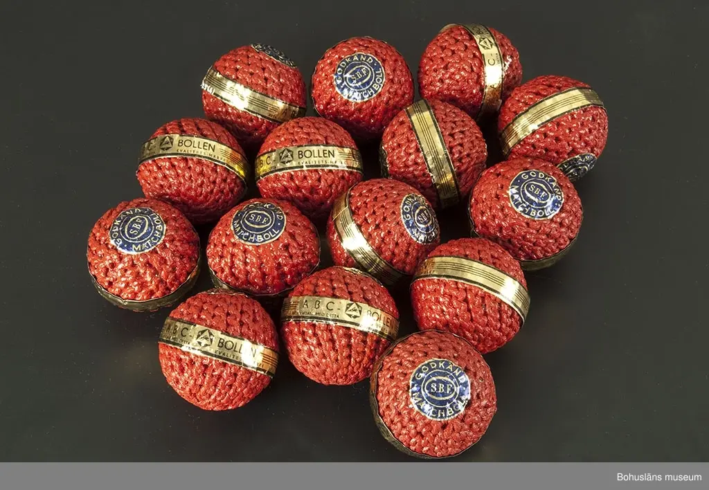 Rödmålade bandybollar med originaletikett.
Samtliga bollar fabriksnya och oanvända. De är försedda med pappersremsa i svart och guldfärg med texten: "ABC-BOLLEN. Äkta endast med detta kvalitetsmärke" och ABC-fabrikernas logotyp samt en cirkelrund lapp i blått med guldtext: "Godkänd matchboll SBF". SBF= Svenska Bandyförbundet.

Tillverkningen skedde delvis som hemarbete. Runt en limmad korkkärna syddes med snören en fast rund form. Dessa "halvfabrikat" hämtades in till fabriken av springpojkar som cyklade runt på paketcyklar. Bollarna doppades därefter i röda färgbad. En del bandybollar doppades också i lack så att de skulle bli riktigt hårda.

Bandyn har i Västsverige varit dominerande bland vinterislagspelen under stora delar av 1900-talet.

Första katalogen med företagets produkter kom år 1911. Där fanns seldon, fotbollar, benskydd och slungbollar presenterade. Redan i 1915 års katalog dyker bandyklubbor och bandybollar upp.

ABC-fabrikerna (Aktiebolaget Bröderna Claesson) hade en omfattande tillverkning av sport- och fritidsartiklar. Under en tid var de Nordeuropas största tillverkare.

Bollarna är inköpta på Lions Loppmarknad i Vänersborg hösten 1995.