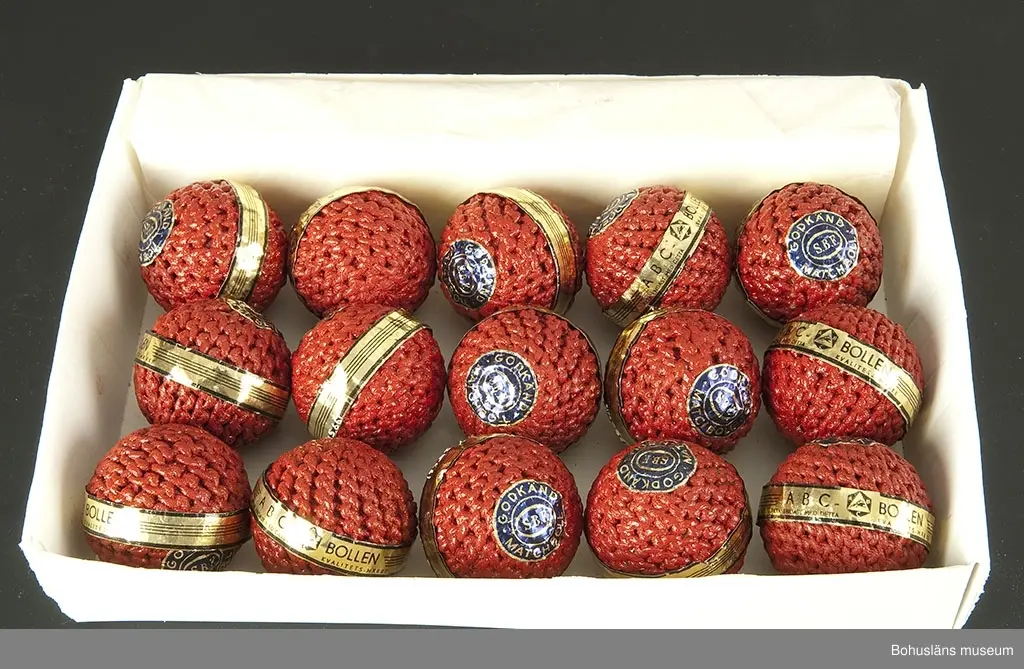 Rödmålade bandybollar med originaletikett.
Samtliga bollar fabriksnya och oanvända. De är försedda med pappersremsa i svart och guldfärg med texten: "ABC-BOLLEN. Äkta endast med detta kvalitetsmärke" och ABC-fabrikernas logotyp samt en cirkelrund lapp i blått med guldtext: "Godkänd matchboll SBF". SBF= Svenska Bandyförbundet.

Tillverkningen skedde delvis som hemarbete. Runt en limmad korkkärna syddes med snören en fast rund form. Dessa "halvfabrikat" hämtades in till fabriken av springpojkar som cyklade runt på paketcyklar. Bollarna doppades därefter i röda färgbad. En del bandybollar doppades också i lack så att de skulle bli riktigt hårda.

Bandyn har i Västsverige varit dominerande bland vinterislagspelen under stora delar av 1900-talet.

Första katalogen med företagets produkter kom år 1911. Där fanns seldon, fotbollar, benskydd och slungbollar presenterade. Redan i 1915 års katalog dyker bandyklubbor och bandybollar upp.

ABC-fabrikerna (Aktiebolaget Bröderna Claesson) hade en omfattande tillverkning av sport- och fritidsartiklar. Under en tid var de Nordeuropas största tillverkare.

Bollarna är inköpta på Lions Loppmarknad i Vänersborg hösten 1995.