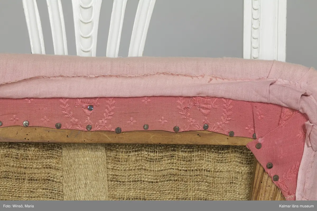 KLM 12727:2. Stol, ryggbrickstol av trä. 8 st. Två något olika grupper av stolar med fyra av varje, den ena gruppen med förgyllda detaljer och den andra helt vitmålad. I övrigt likadan dekor. Den ena gruppen stolar (stol 1-4) är vitmålade med guldfärgad äggstavsdekor på fram- och sidosargarna. Dekor på ryggöverstycke samt framsarg i form av humlekvistar. Benen är kannelerade, delvis förgyllda och nedåtavsmalnande. Ryggbrickan är genombruten och har en form av ett kopplat spjälknippe. Sitsen är stoppad och klädd med textil med ränder med blomsterslingor. Textilen är mycket blekt och originalfärgen syns på några ställen, då i grönt. Gruppen med stolar som är utan förgyllning (stol 5-8) har tidigare haft sitsarna klädda med rosa textil med mönster av lagerkransar med urna i mitten. Likadan textil kan ses på dyna i soffan KLM 27787. Gustaviansk.