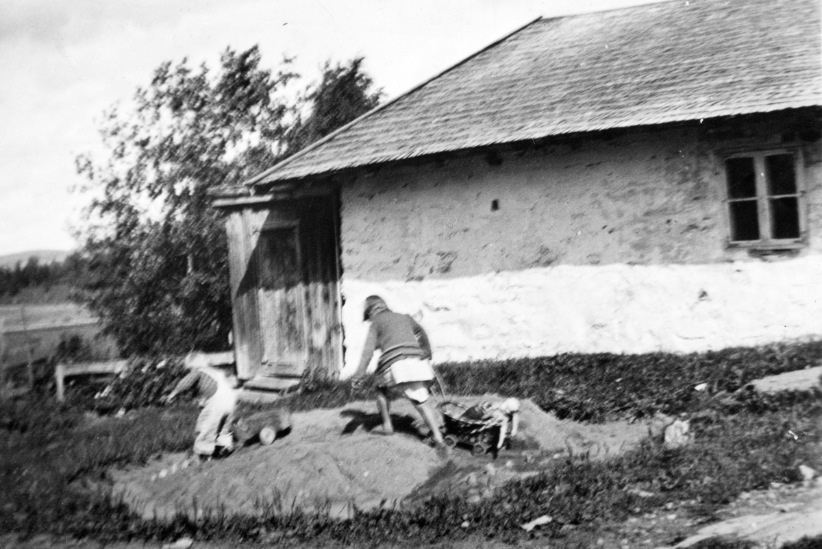 I sandhaugen foran gammelfjøset på Søndre Tomter (Ner-Tomter) i 1934. Marta H. med dokkevogn og Harald M. med lekebil.