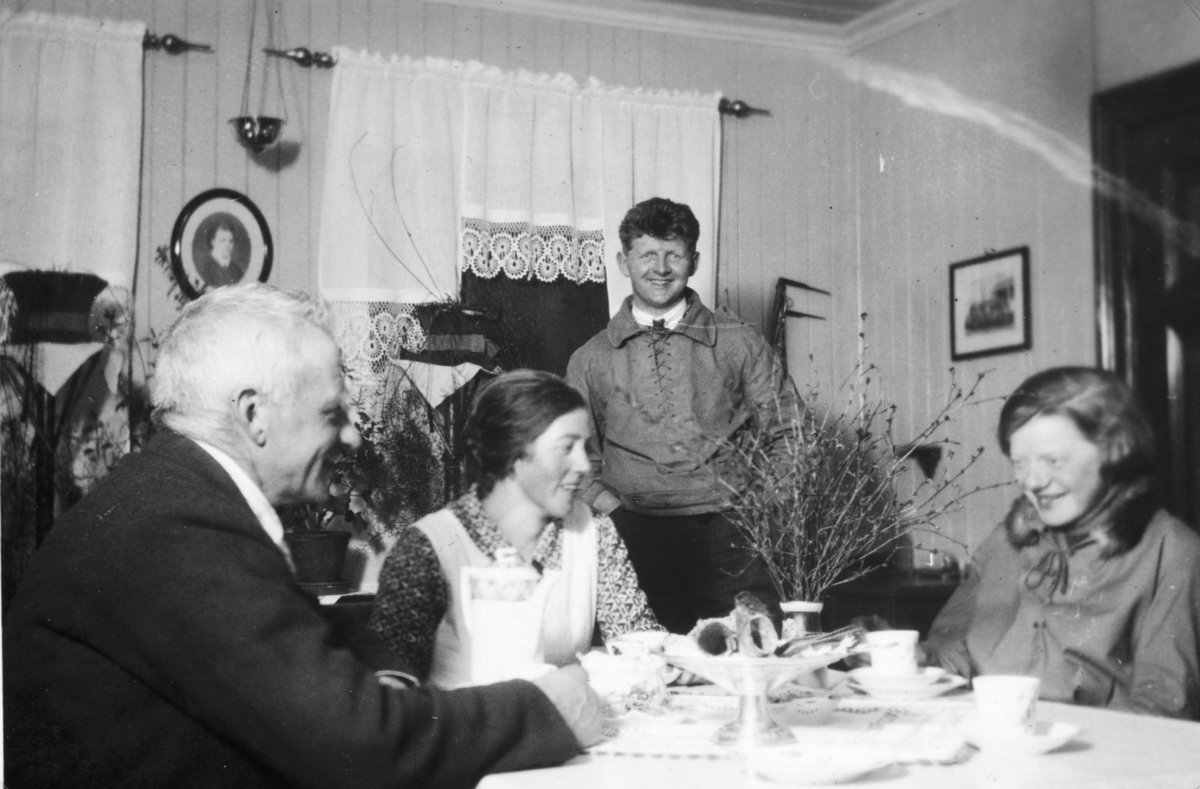 Fra dagligstua på Søndre Tomter (Ner-Tomter). Jacob og Helga Tomter har kaffegjester som hadde lånt hytta på setra på Tørbustilen. Mellom vinduene henger bilde av Jacobs mor Karen f. Imerslund. I hjørnet under vinduet sår skrivebordet til gardbrukeren Jacob. Over skrivebordet henger tømmerklaven.