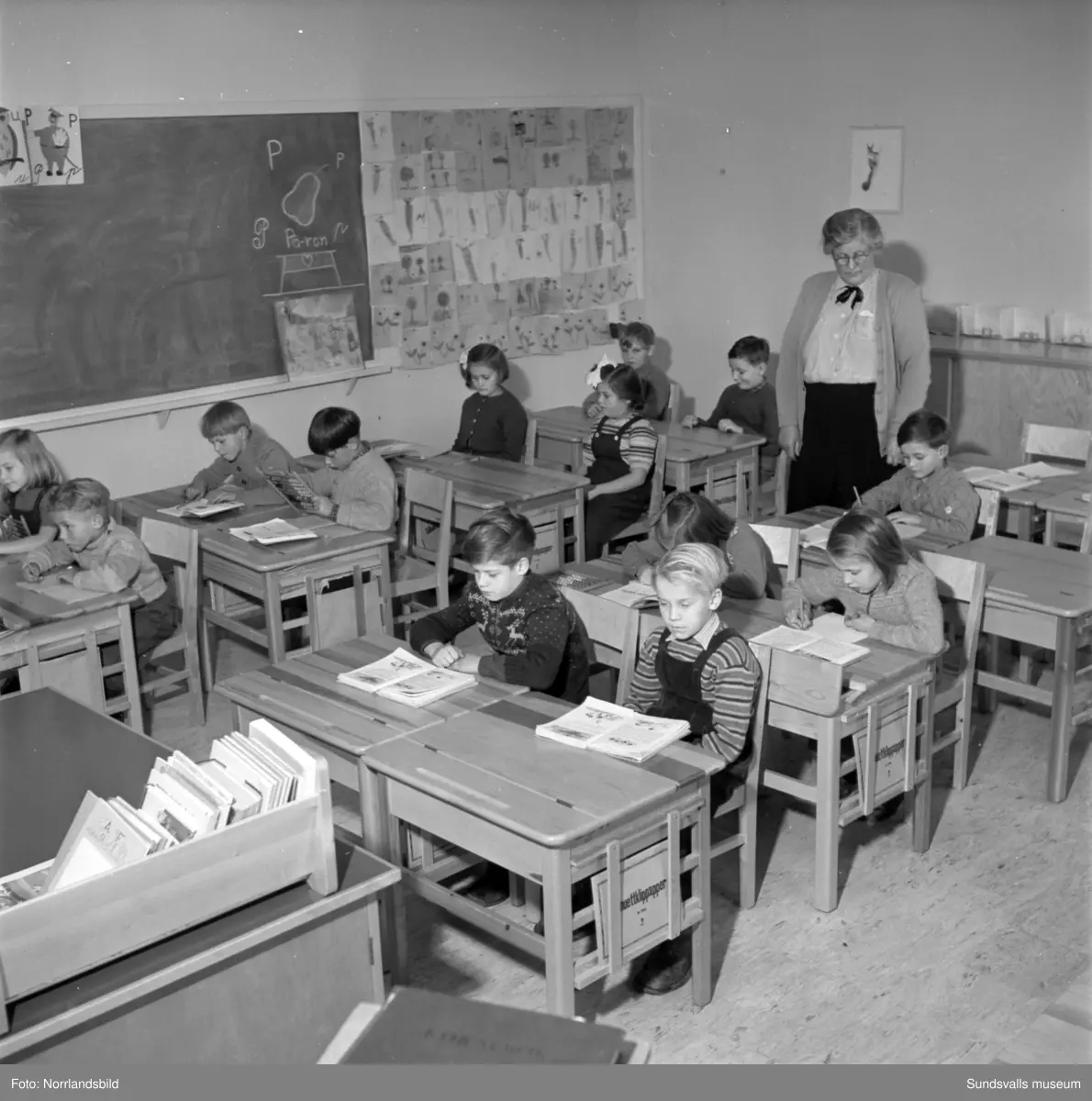 Reportagebilder från Stöde skola, tidigare Slättåbygdens skola. Exteriör, interiör, lektioner i klassrummen, rastlek, elever, personal, lärarrum och affischförråd. Bild 2: busschauffören är Jonas Malmgren. Bild 8: Harry Wiberg. Bild 9: Maritta Larsson. Bild 12: vaktmästare Adrian Almgren. Bild 14: Johan Näsström. Bild 15: Lärarrummet med: Längst bak från vänster Karin Jonsson, Linnea Sterner, Roland Källsäter och Johan Näsström. Längst fram sitter Märta Näsström och Hildegard Svensson.