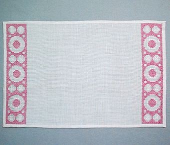 Tablett SNÖBÄR i linne broderad i korsstygn. Mönstret, i form av cirklar och ringar, är placerat som en bård i var kortsida och lämnar mittfältet tomt. Blekt/vit linneväv med broderi i rosa lingarn.
