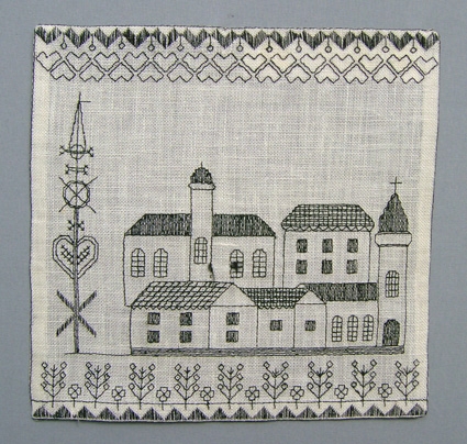Väggprydnad MAJSTÅNG i form av broderad bild på vitt linne. Bilden föreställer konturer av en stad med en majstång och en bård med blommor nertill . Broderat med svart lingarn i rutsöm och dubbla förstygn.