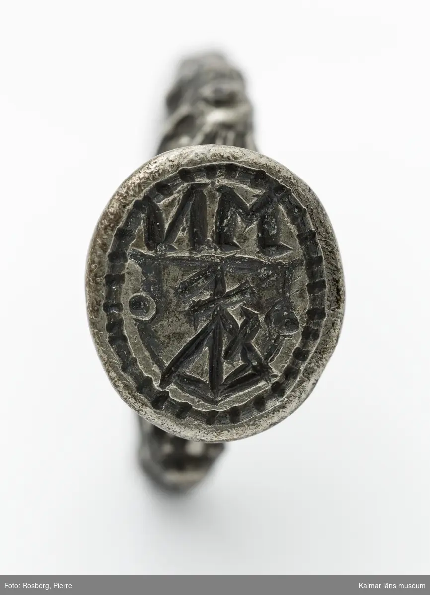 KLM 16729. Sigillring, av silver. Trind ring, oval tjock klack. Renässansornament i övergången mellan ring och klack. I klacken bokstäverna MN samt vapensköld med bomärke. Datering: 1500-tal eller tidigt 1600-tal.