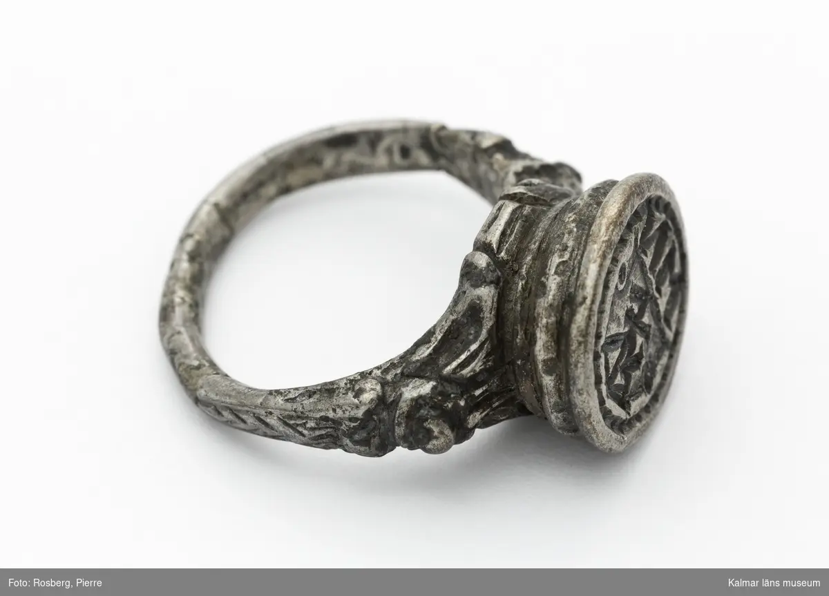 KLM 16729. Sigillring, av silver. Trind ring, oval tjock klack. Renässansornament i övergången mellan ring och klack. I klacken bokstäverna MN samt vapensköld med bomärke. Datering: 1500-tal eller tidigt 1600-tal.