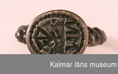 KLM 16729. Sigillring, av silver. Trind ring, oval tjock klack. Renässansornament i övergången mellan ring och klack. I klacken bokstäverna MN samt vapensköld med bomärke. Datering: 1500-tal eller tidigt 1600-tal.