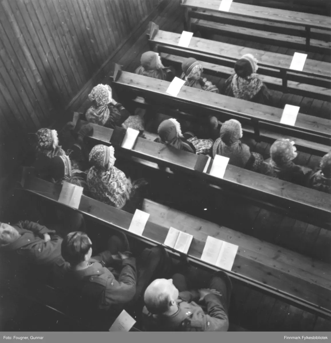 Inne i Karesuando kirke. Folk sitter på benkene. Vi ser militære menn i uniform og samer i samedrakter. Bildet er tatt fra galleriet.

Begravelse av to soldater som omkom under brøyting av vei vinteren 1945. Den ene var Norsk soldat og den andre var Svensk. Dagboksnottater til Henry W. Hadeland sier at han ikke ble funnet og kisten med det Svenske flagget er tom. 

Soldatene som døde, var en del av pionertroppene. Pionertroppene besto av soldater fra fra bataljon I og V pluss en gruppe tropp, i tillegg til 3.rikspolitikompani og et bilkompani, senere R.P.-bataljon I under major Mølster og til sist de to gjenværende kompaniene fra bataljon II. 

Arbeidet med å brøyte og anlegge veien ble ledet av en svensk ingeniøroffiser, major A. Welin og man engasjerte en del svenske veispesialister til å hjelpe til med brøytingen med 3-tonns traktorer og fikk også lånt to 5-tonns traktorer fra Sverige. 

Brøyting av vei tvers over den finske kilen, fra Karesuando til Kautokeino hadde to hensikter, både militært og sivilt nødvendig. I området oppholdt det seg en mengde sivile som var berøvet alt de hadde og som var helt henvist til hjelp fra andre steder. Formålet militært var å rykke frem til Kautokeino, opprette en fast basis, en forsyningsstasjon der og så rykke videre mot Alta og Reisenfjord. Veien ble lagt der terrenget var lettest, fortrinnsvis på sjøer og langs elvedrag. 

Det var under dette arbeidet at en av traktorene gikk gjennom isen og to mann druknet. 

Se også FBib.93189-004 og FBib.93189-005.