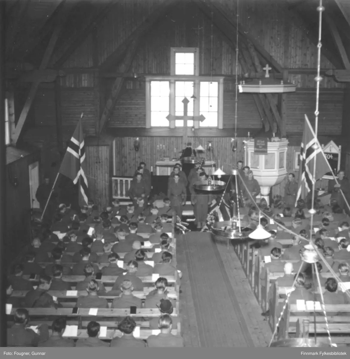 Begravelse av to (norsk og svensk) soldater som omkom under brøyting av vei vinteren 1945. Fotografert inne i Karesuando kirke. 12 soldater står klare til å bære ut kistene. Den ene var Norsk soldat og den andre var Svensk. Dagboksnottater til Henry W. Hadeland sier at han ikke ble funnet og kisten med det Svenske flagget er tom. Det ser hvitt ut på s/h-bildene. Flagget er stort. 

Soldatene som døde, var en del av pionertroppene. Pionertroppene besto av soldater fra fra bataljon I og V pluss en gruppe tropp, i tillegg til 3.rikspolitikompani og et bilkompani, senere R.P.-bataljon I under major Mølster og til sist de to gjenværende kompaniene fra bataljon II. 

Arbeidet med å brøyte og anlegge veien ble ledet av en svensk ingeniøroffiser, major A. Welin og man engasjerte en del svenske veispesialister til å hjelpe til med brøytingen med 3-tonns traktorer og fikk også lånt to 5-tonns traktorer fra Sverige. 

Brøyting av vei tvers over den finske kilen, fra Karesuando til Kautokeino hadde to hensikter, både militært og sivilt nødvendig. I området oppholdt det seg en mengde sivile som var berøvet alt de hadde og som var helt henvist til hjelp fra andre steder. Formålet militært var å rykke frem til Kautokeino, opprette en fast basis, en forsyningsstasjon der og så rykke videre mot Alta og Reisenfjord. Veien ble lagt der terrenget var lettest, fortrinnsvis på sjøer og langs elvedrag. 

Det var under dette arbeidet at en av traktorene gikk gjennom isen og to mann druknet. 

Se også FBib.93189-003 og FBib.93189-004.

