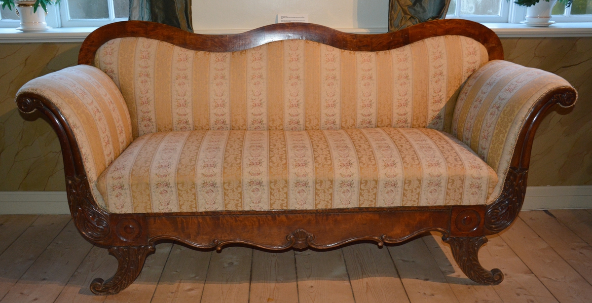 Rektangulær sofa med treramme rundt hele formen.Beina er skrådd utover med dekor av blad i treskjæring. Utskjæringer også foran og på armlenene. Treverket på ryggen er helt glatt. Trerammen er lakkert. Sofaen er stoppet,tøyet er delt inn i langsgående blomsterornamentikk.