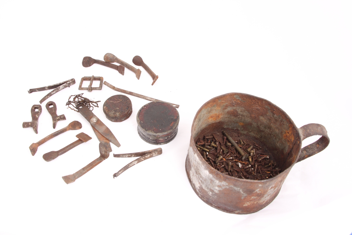 En metallkopp med ulike gjenstander. 
Koppen inneholder; en beltespenne, to runde metallbokser, tre pinsetter, diverse nøkler(?), tråd til beksøm(?) og skruer i ulik størrelse.