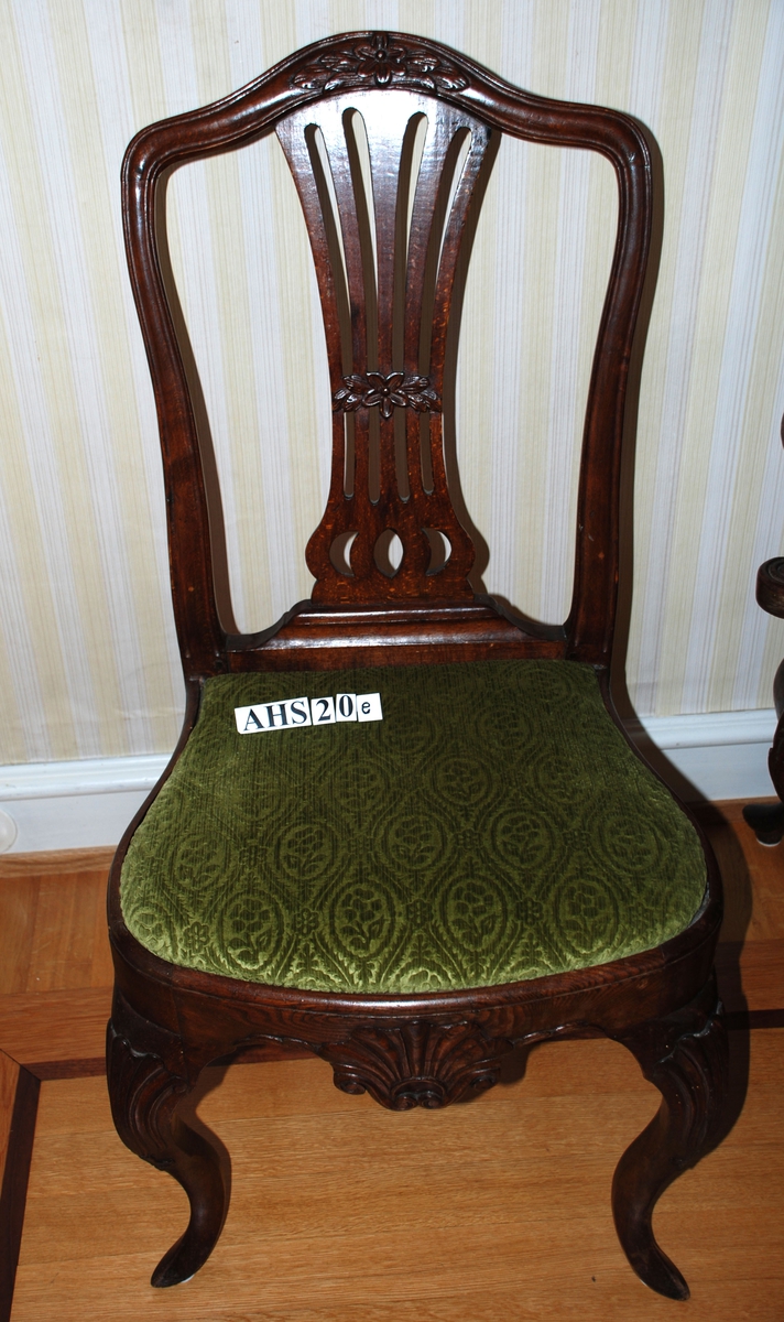 Overgang fra rokokko til klassisisme. Stol i bonet bøk. Slanke bukkeben med skjell på kneet og spiss fot. Sargen rundet ved knærne og med stort symetrisk skåret skjell på midten. Ryggen Hepplewhite-type. Midtfjelen 5 spiler "bundet sammen" på midten ved et bånd av blomster og blader skåret i relieff. Topplisten, som går jevnt over fra sidestavene går opp i en bue, på midten prydet med blomster og blader skåret i relieff. Trukket med grønt tekstiltrekk.