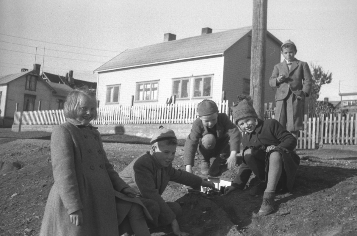 Flere barn leker ute i Nyborgveien i Vadsø. Noen av dem er, fra venstre: Erna (Tulla) Haldorsen, Rolf Hauge, ukjent, Edel Haldorsen (en yngre søster av Erna Haldorsen), og en ukjent gutt står litt bak ved stolpen.