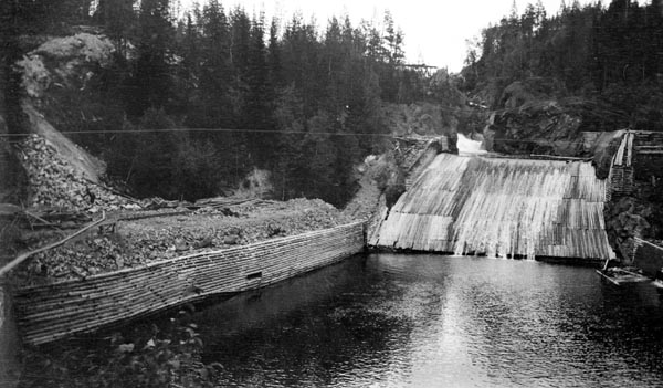 Osfallet i elva Søndre Osa i Åmot kommune i Hedmark.  Fotografiet er tatt da kraftutbyggingsarbeidet var i startfasen, antakelig sommeren 1913.  I forgrunnen ser vi kulpen under fallet og det nederste av de to, til sammen 25,5 meter høye fallene som skulle gi hydroelektrisk energi både til belsyning i mange hjem i den sentrale delen av Åmot kommune og til den nye treforedlingsbedriften som var under etablering like sør for stasjonsbyen Rena.  Det vi ser på dette fotografiet er imidlertid hovedsakelig konstruksjoner som var bygd på oppdrag fra Christiania Tømmerdirektion, en fløtingsorganisasjon som seinere ble en del av Glomma fellesfløtingsforening.  Omkring kulpen nedenfor fallet ser vi at det er bygd skjermer av tømmer i forholdvis stor høyde, for å forhindre at fløtingsvirket ble drevet på land.  Ovenfor ser vi den nerste av de to avsatsene i fallet.  Også den er skjermet med tømmer på begge sider.  Dessuten er det lagt "flakning" eller "golving" - rister av tømmer som lå tett i tett, parallelt med strømretningen.  Poenget med dette var å forhindre at tømmerstokkene ble skadet eller satte seg fast i det opprevne berget på elvebotnen.  Dette fotografiet er tatt ved lav sommervannstand, og da lå mesteparten av golvinga i dagen.  Ovenfor skimter vi kvitskummende vann fra det øvre Osfallet.  I det berglendte landskapet omkring fallet vokste det barskog da dette fotografiet ble tatt.

Mer informasjon om kraftutbygginga ved Osfallet og om det store dambruddet som inntraff i mai 1916 finnes under fanen «Opplysninger».